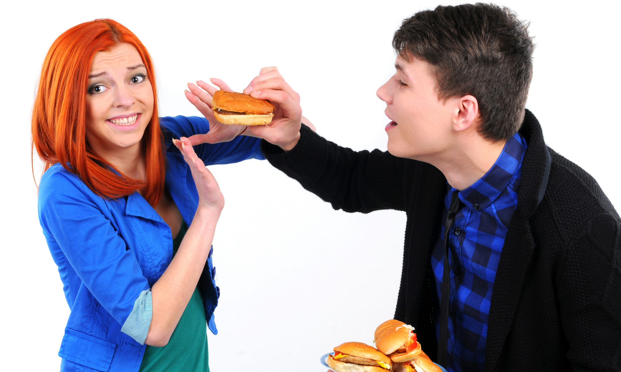 Woman holds up hands in refusal of hamburger aggressively offered by man holding a plate of burgers