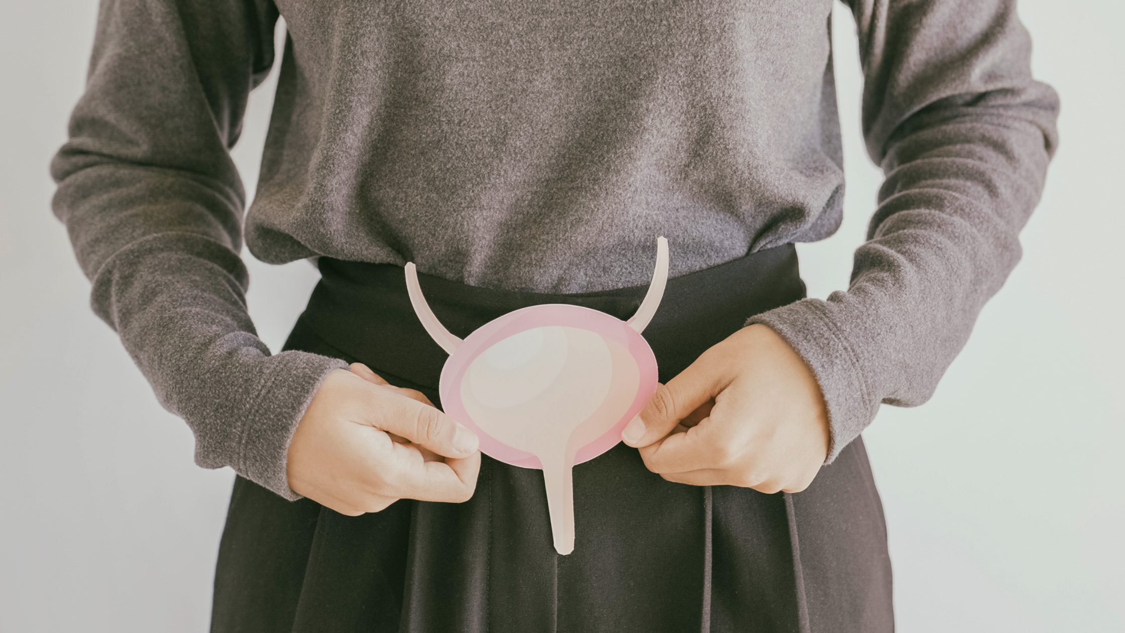 person holding a simple paper illustration of a bladder in front of their pelvis