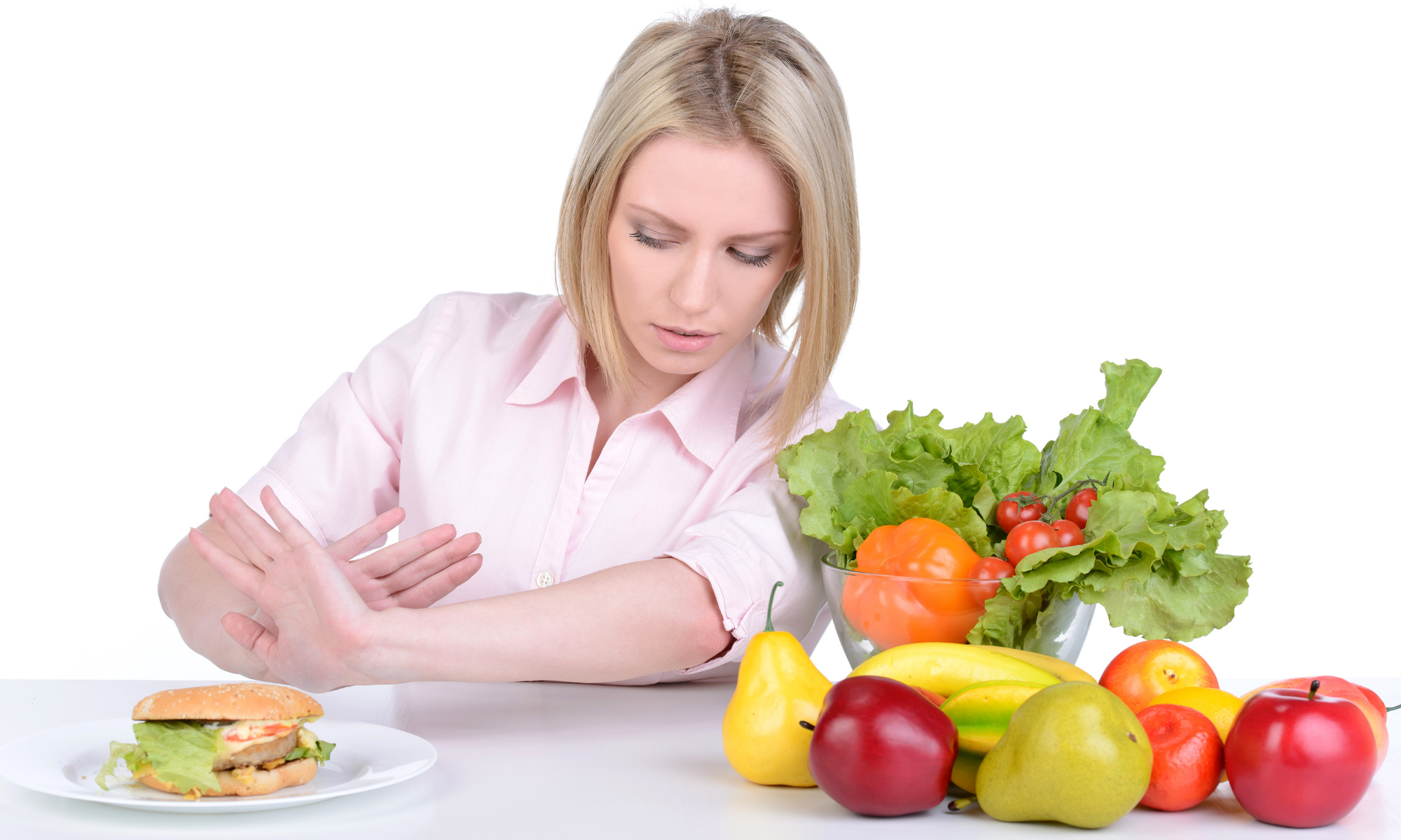 Woman holds out hands in refusal of hamburger on the left while various fruits and vegetables are on the right