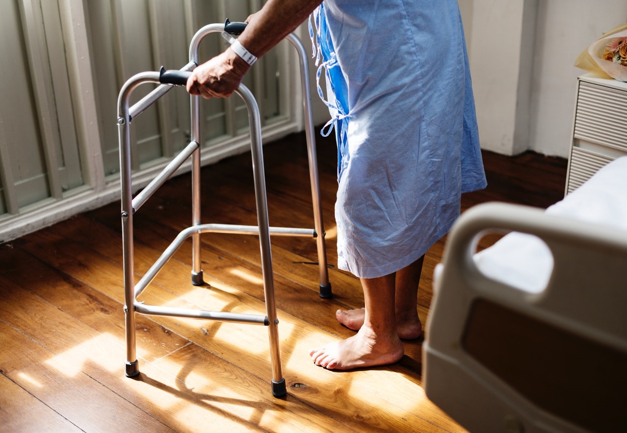 Barefoot senior woman in care center room stepping toward the window with a walker