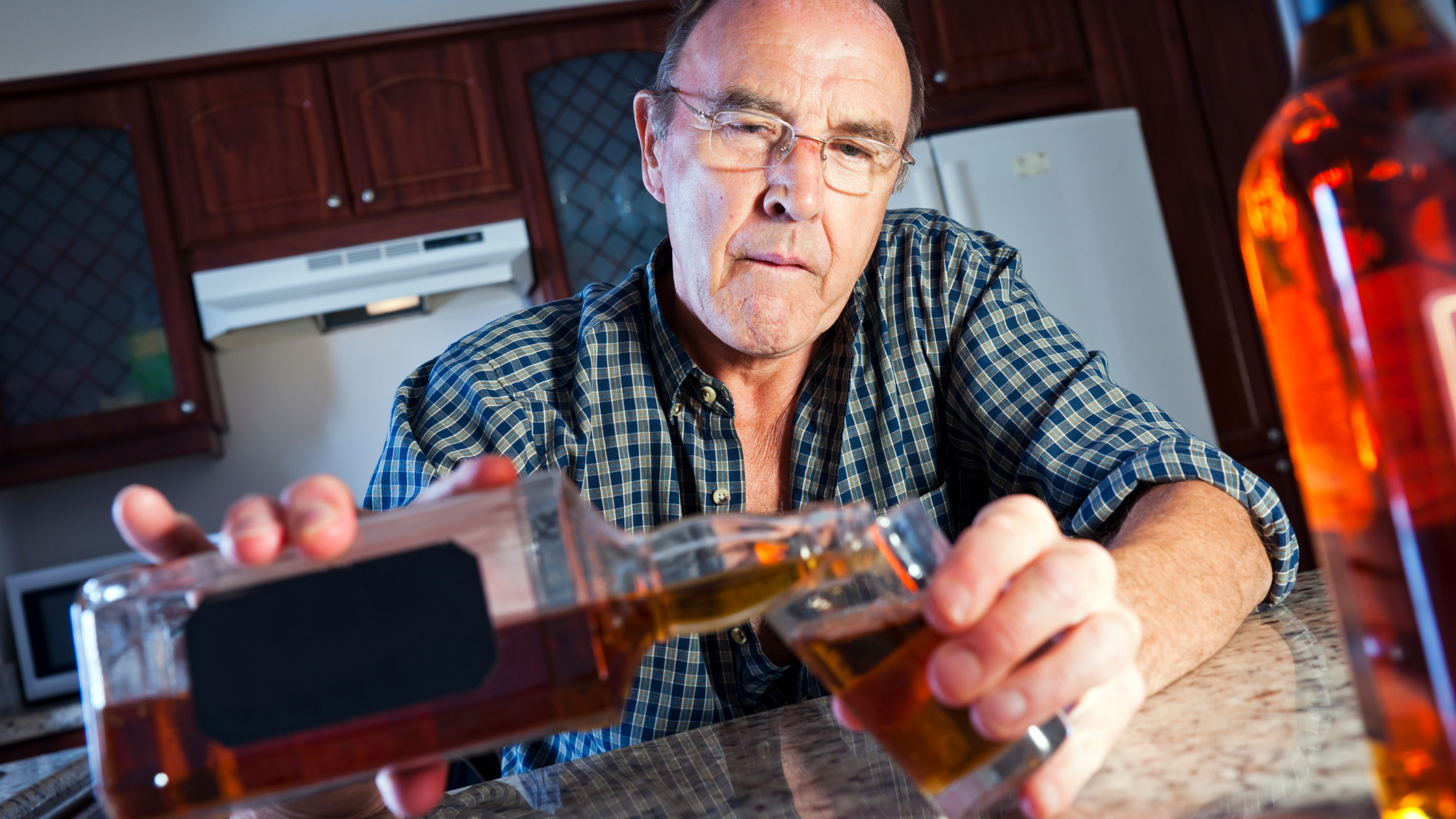 senior man pours himself a large glass of whiskey