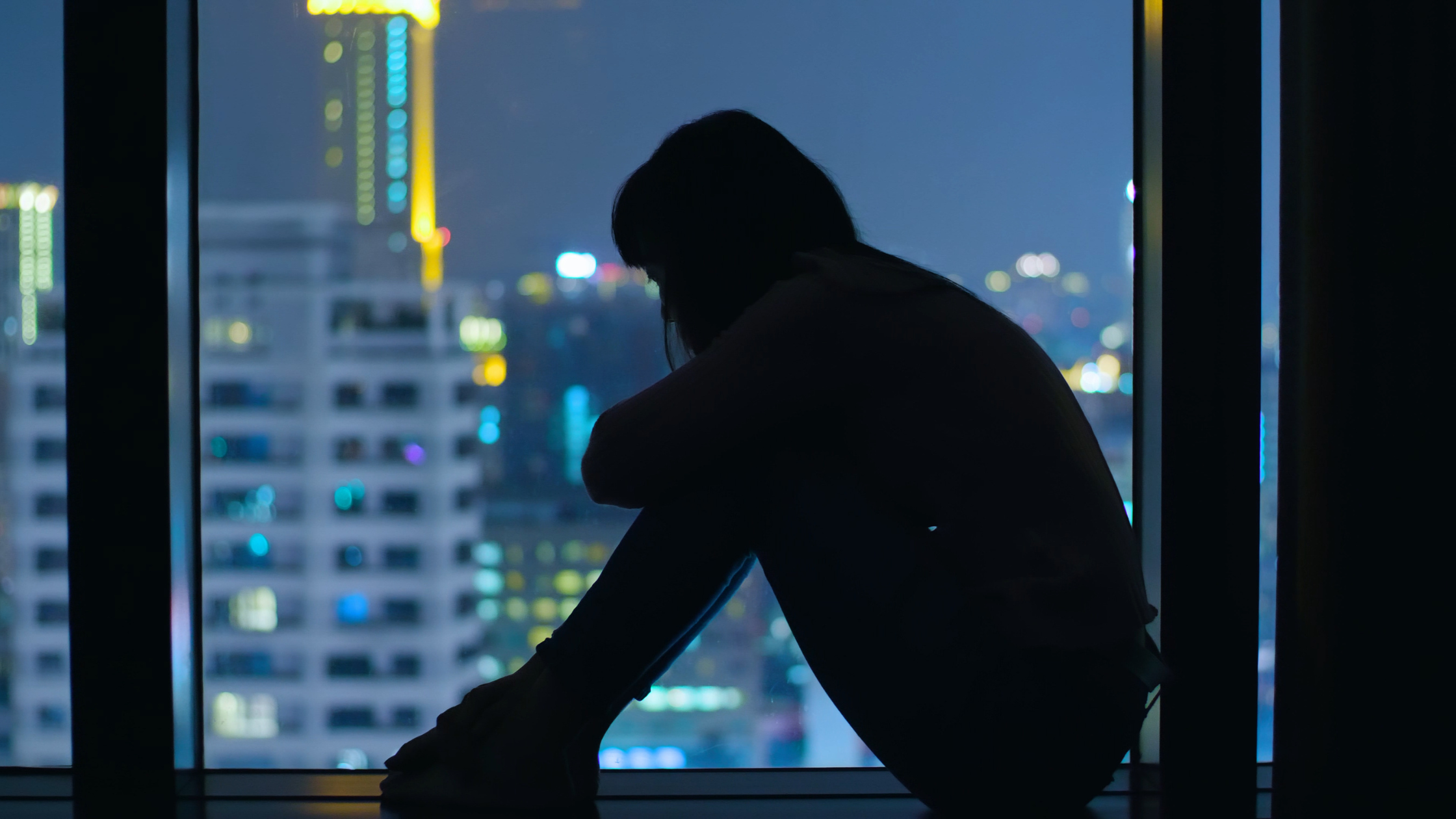 silhouette of a person sitting against a window with a night skyline
