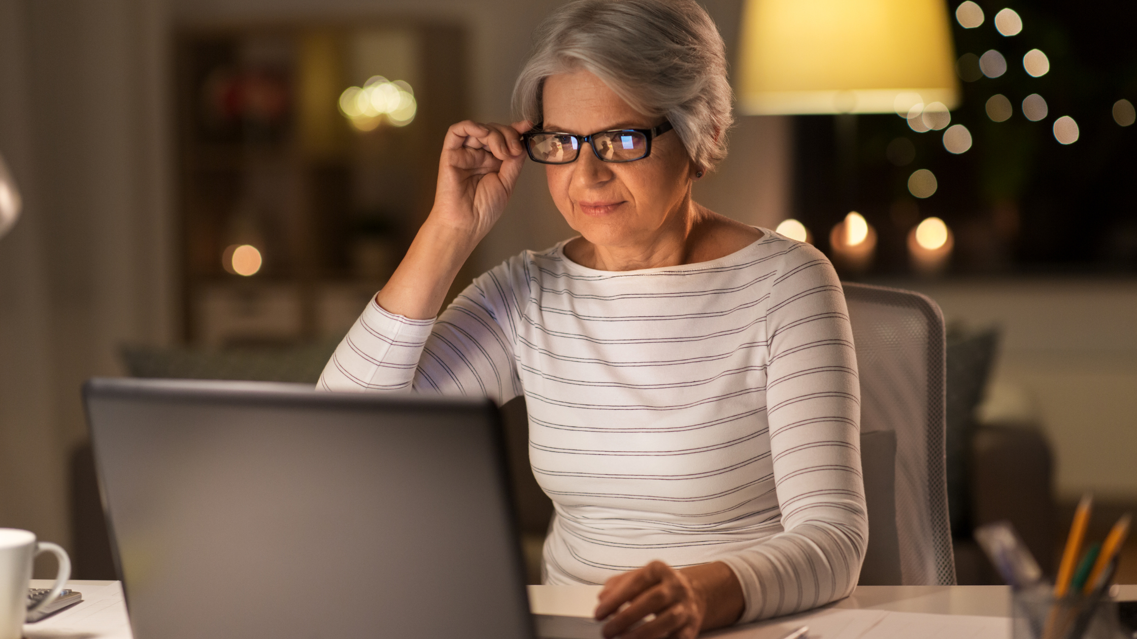 senior woman adjust her reading glasses in front of a computer