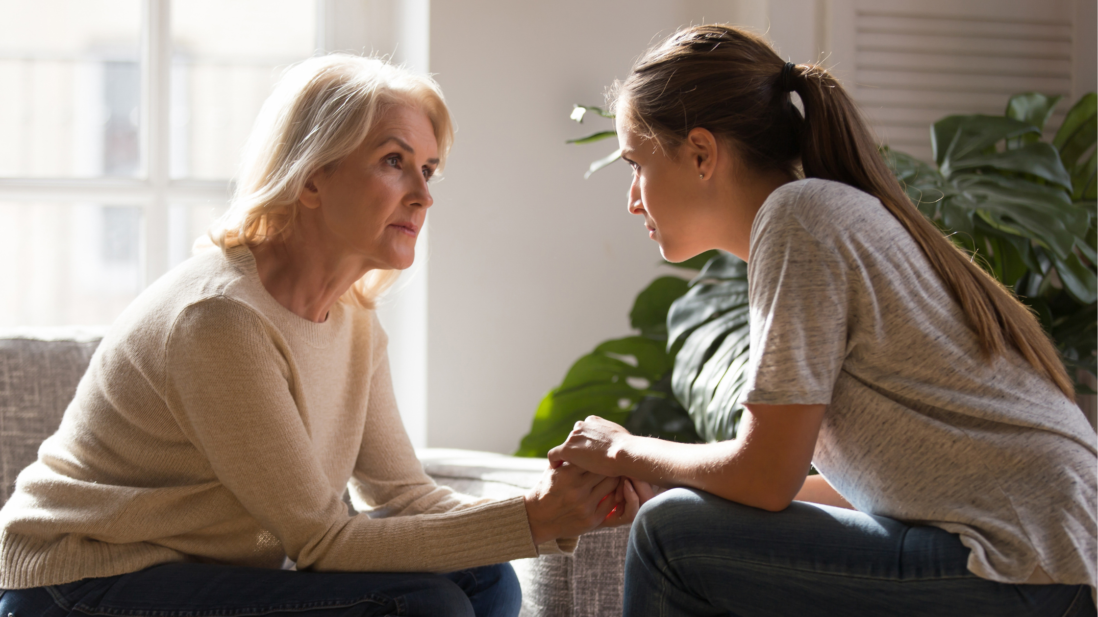 two women sit facing each other with their hands clasped in a serious conversation