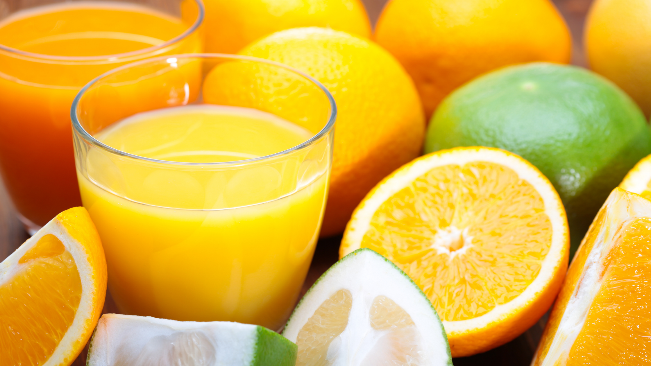 Two glasses of orange juice nestled amongst sliced and unsliced oranges