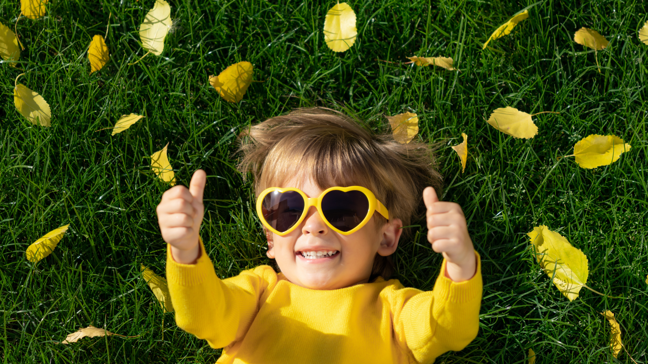 smiling toddler in sunglasses with two thumbs up