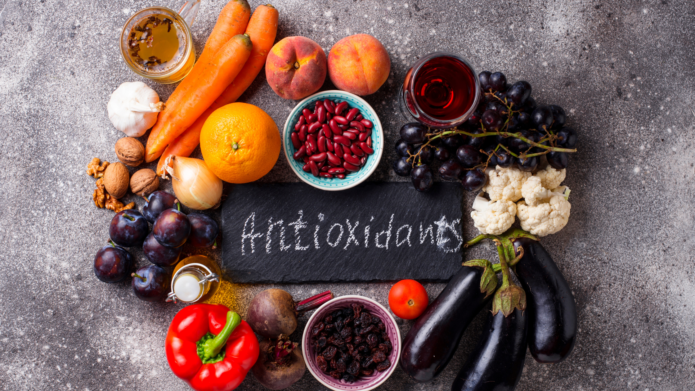 "Antioxidents" written on slate board with chalk, surrounded by fruits and vegetables, pepper, eggplant, grapes, cauliflower, carrots, tangerines