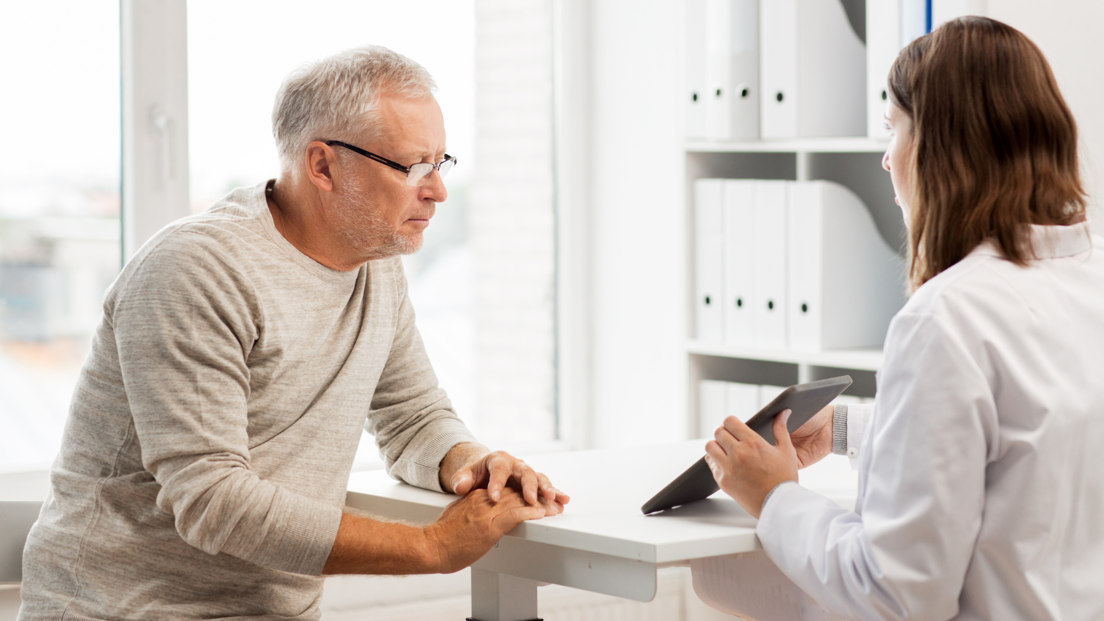 doctor shows senior man something on a tablet while she speaks to him
