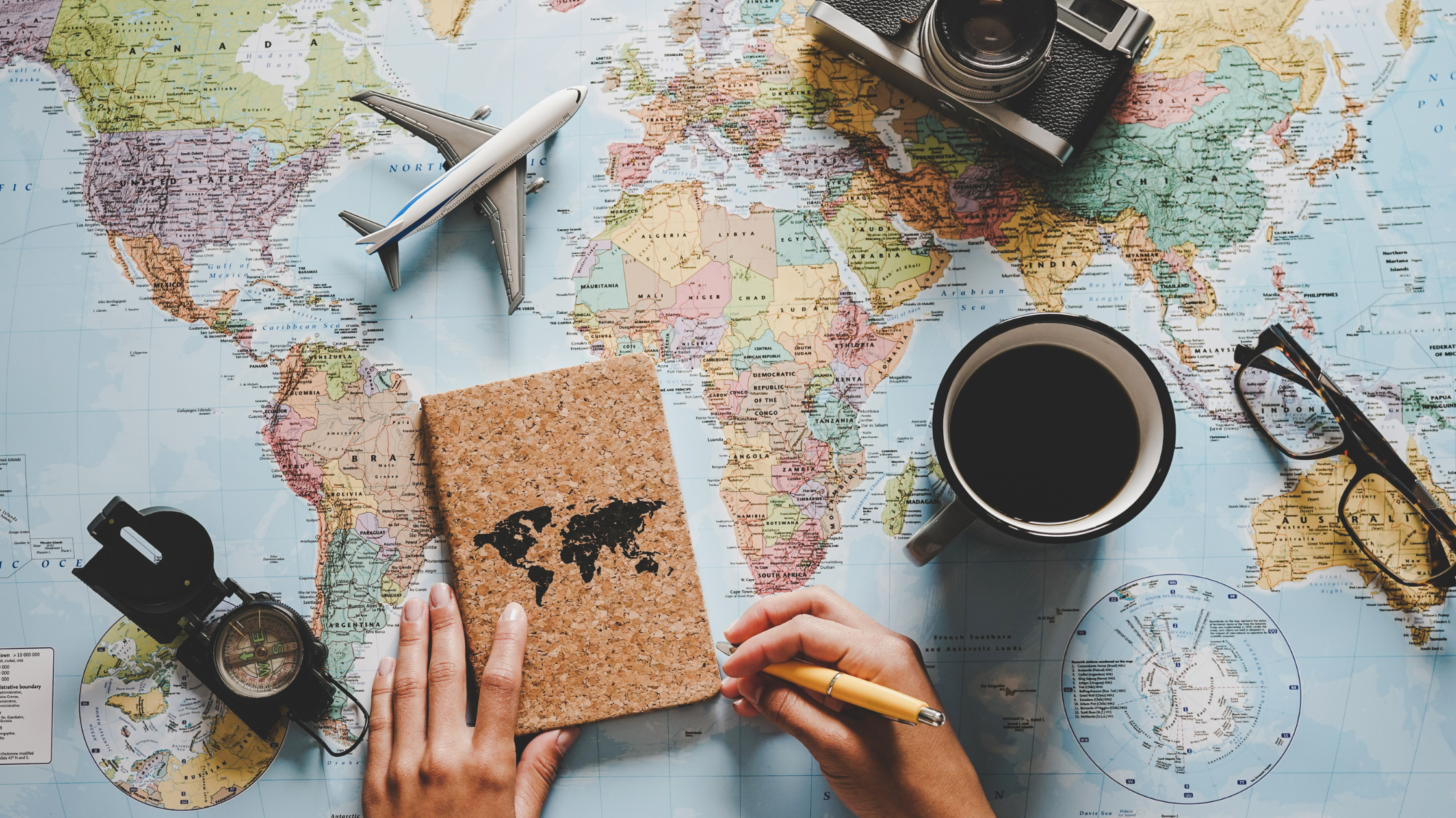 map of the world with a camera, glasses, binoculars, a model plane, and a notebook 