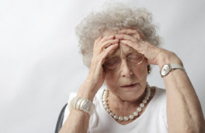 Senior woman with eyes closed anxiously presses her hands to her forehead