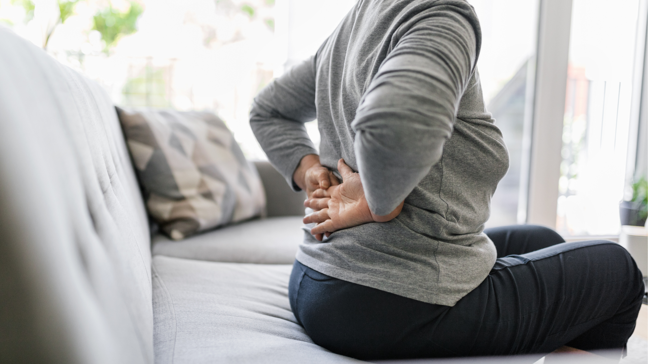 close up of someone sitting on a couch, with their hands pressed against their lower back