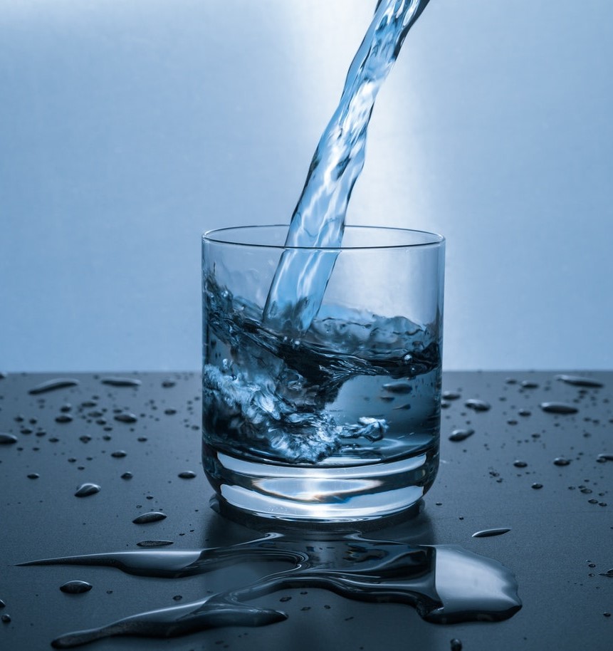 Large stream of water being poured into a glass, splashed water standing on the table around the glass