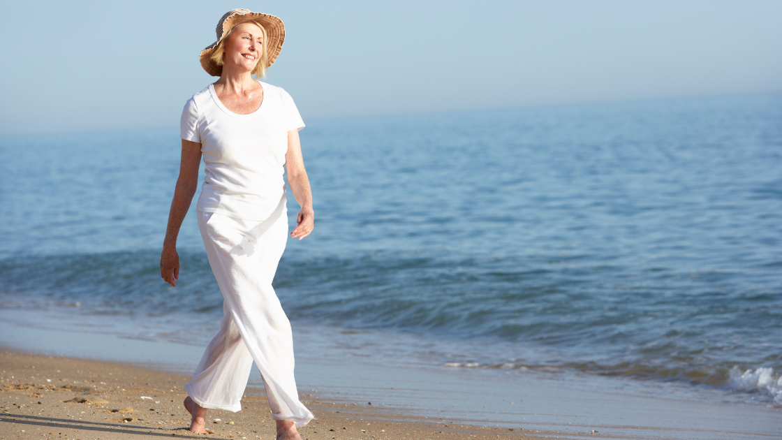 Happy older woman in white walks on the beach