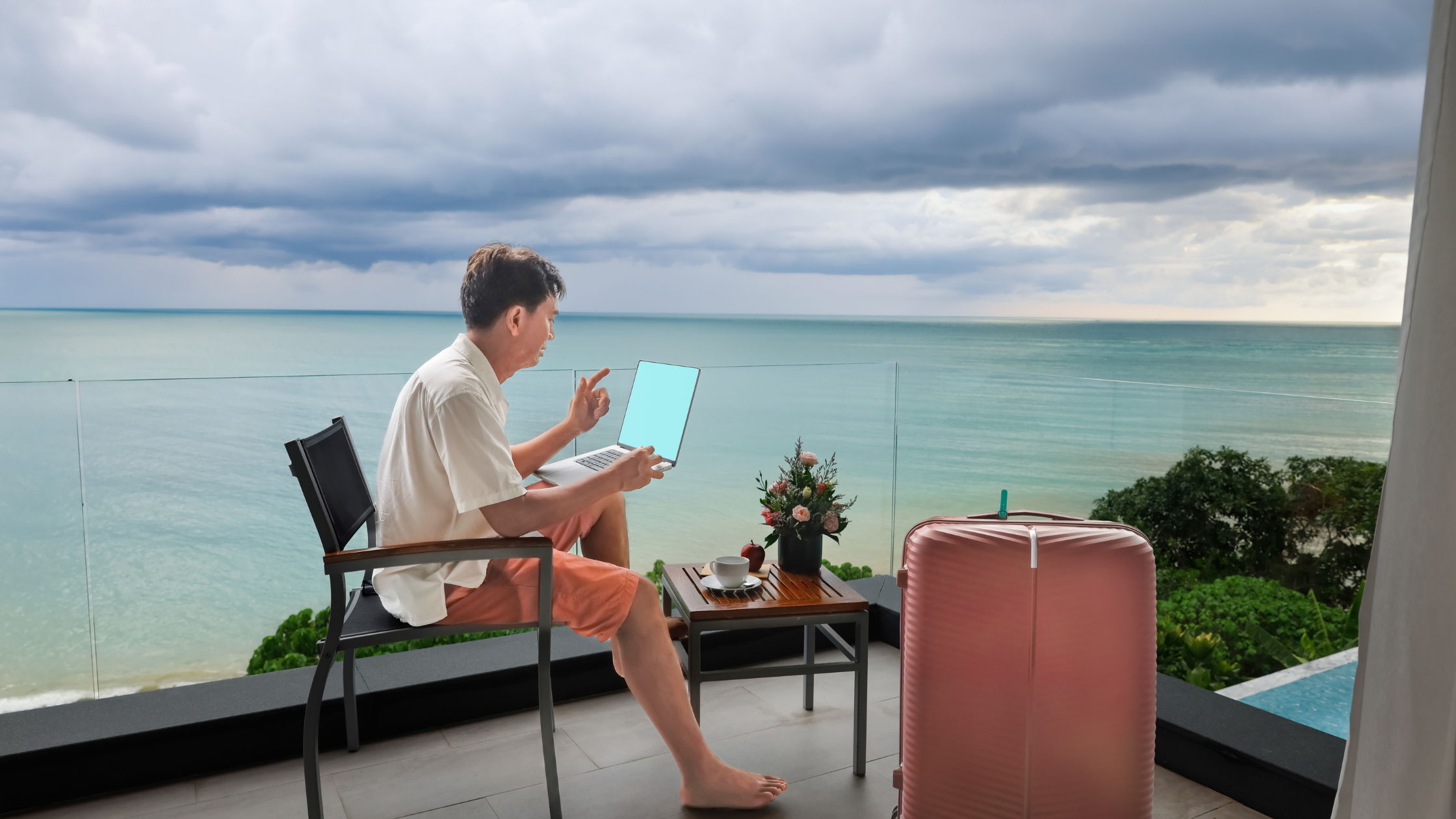 man speaks animatedly to a laptop on a beachside balcony