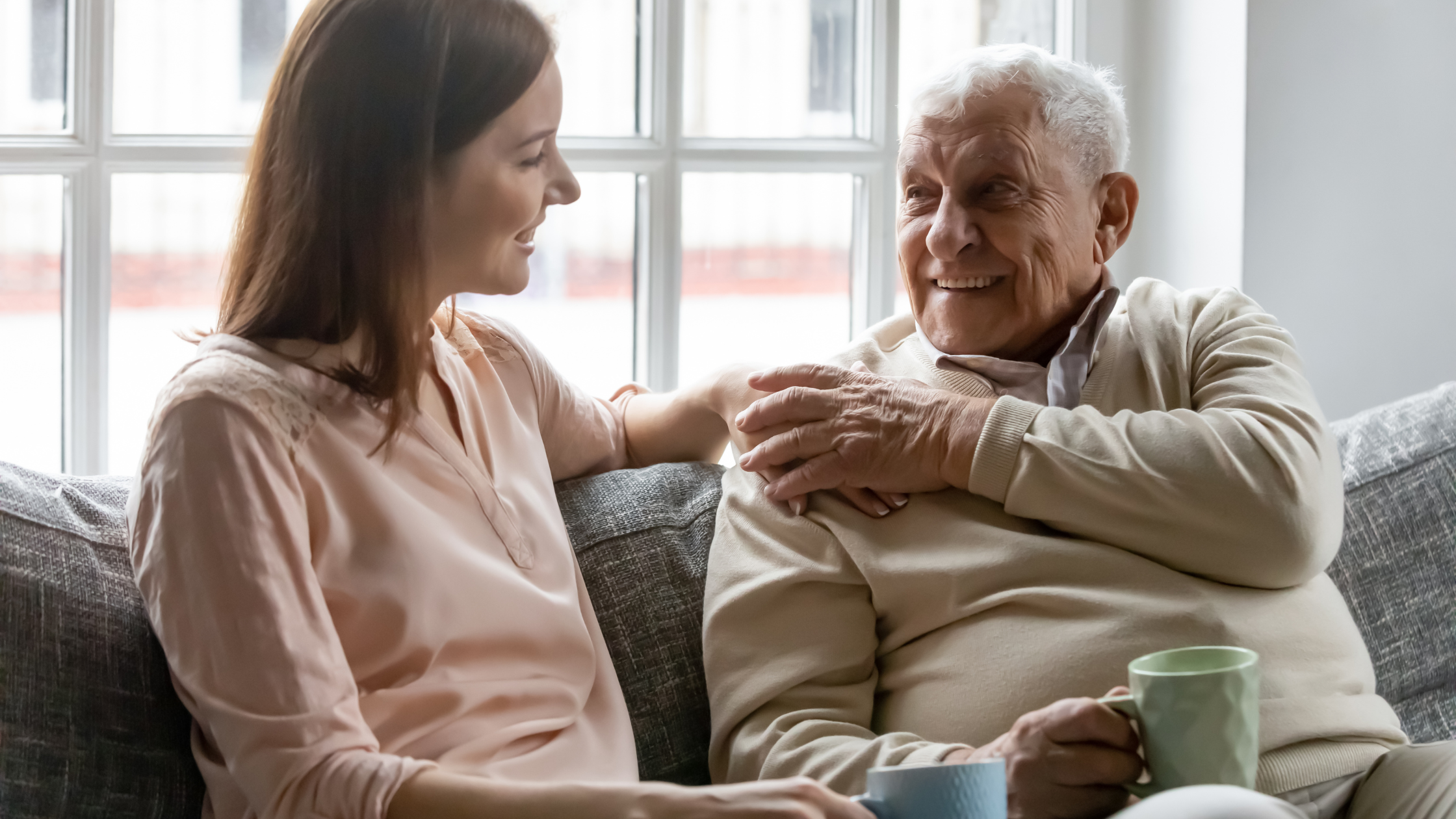 younger woman and senior man sit chatting on a couch