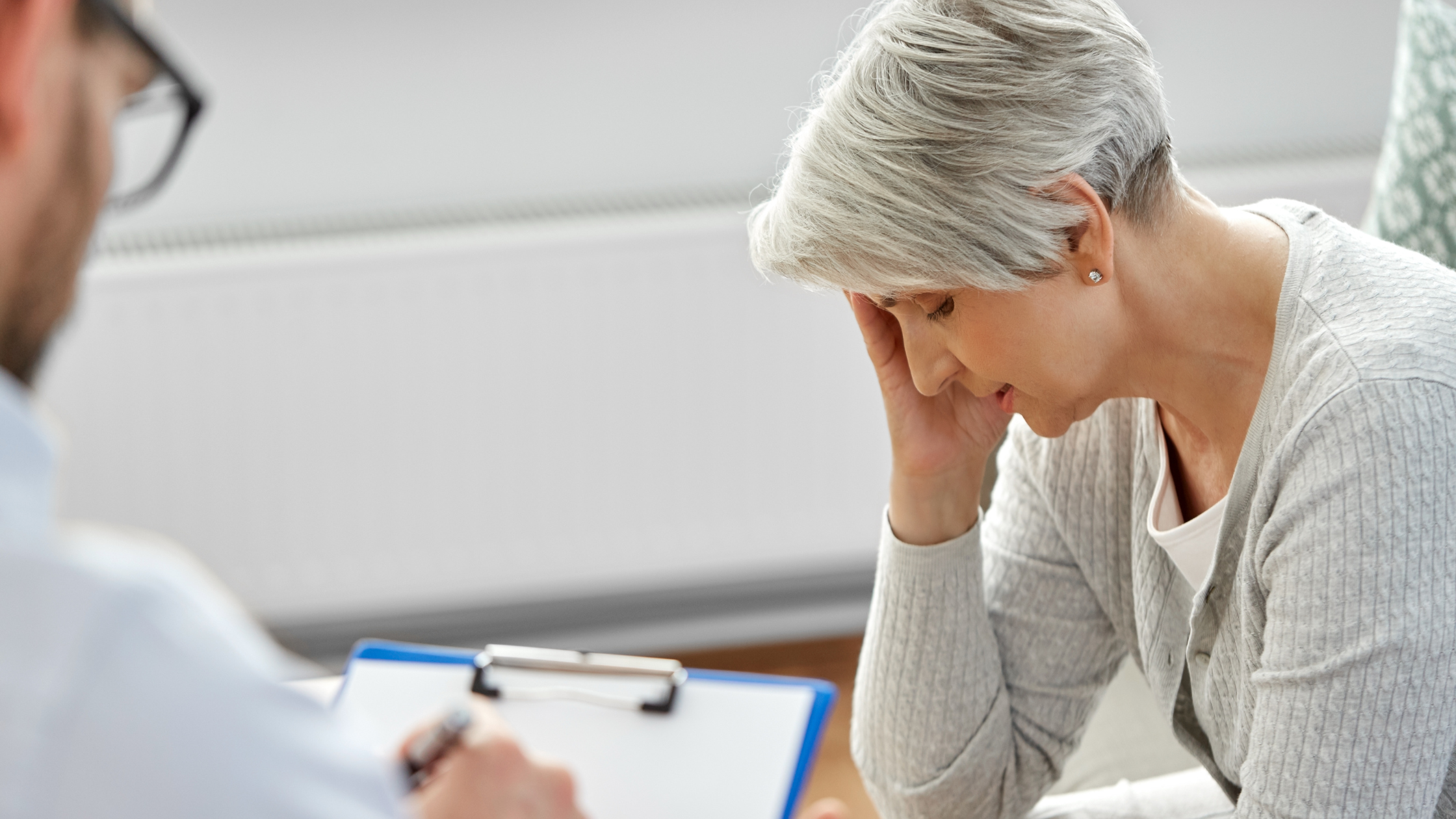 doctor takes notes while a woman with her head in her hand talks