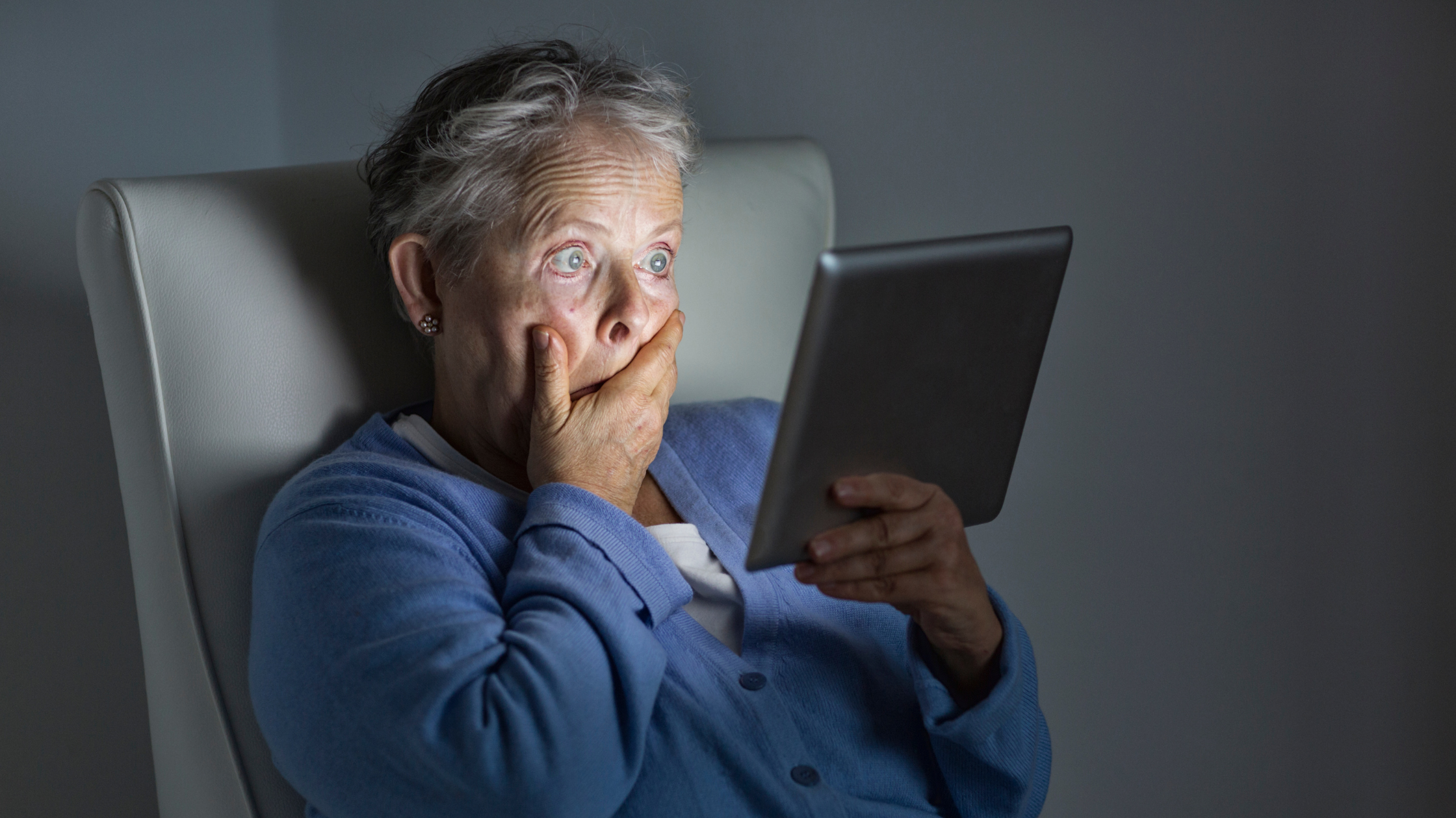 Older lady is surprised at something she is looking at on a tablet, her hand over her mouth
