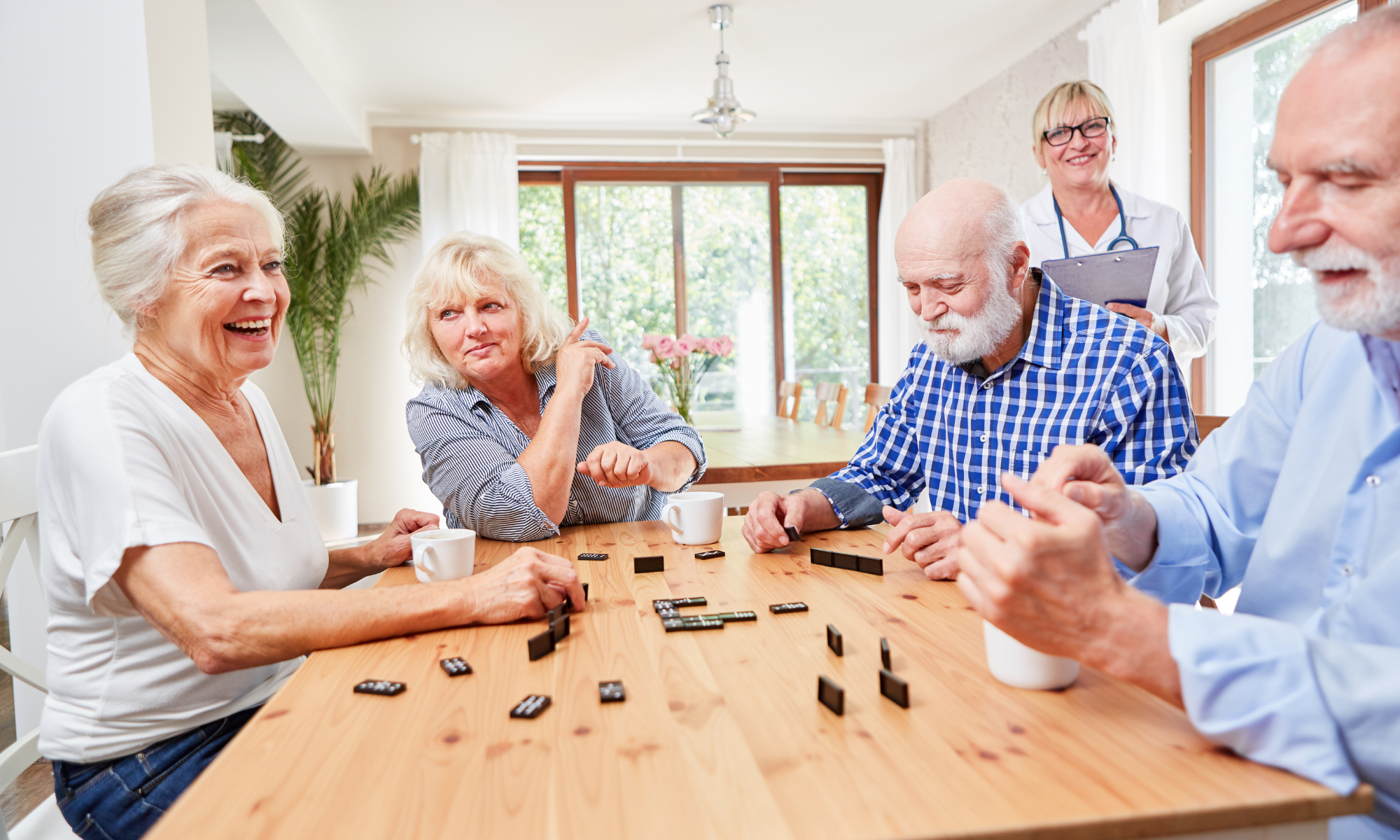 Group of seniors enjoying playing dominoes while a nurse looks on smiling