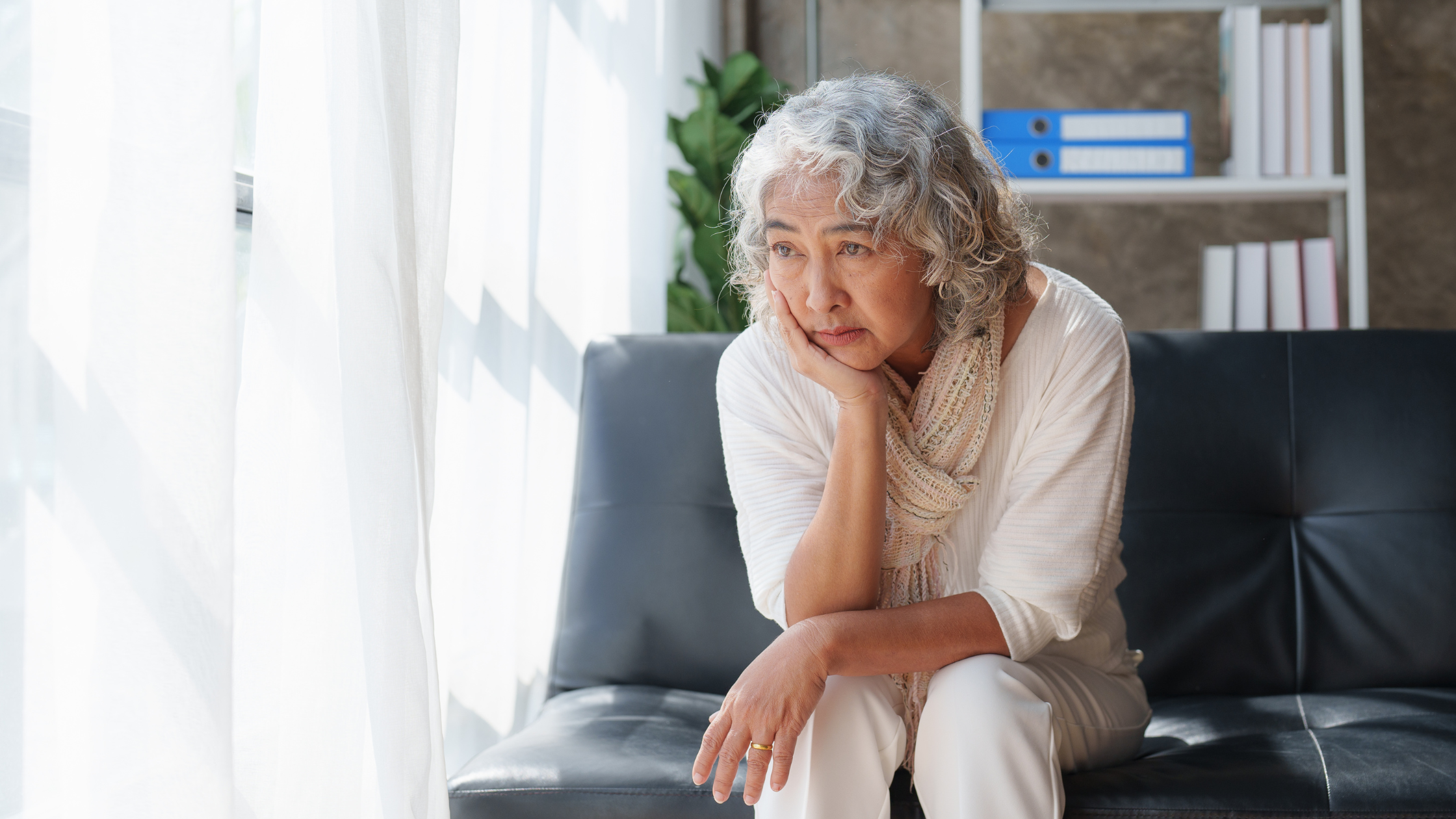 forlorn-looking woman sits on a couch alone