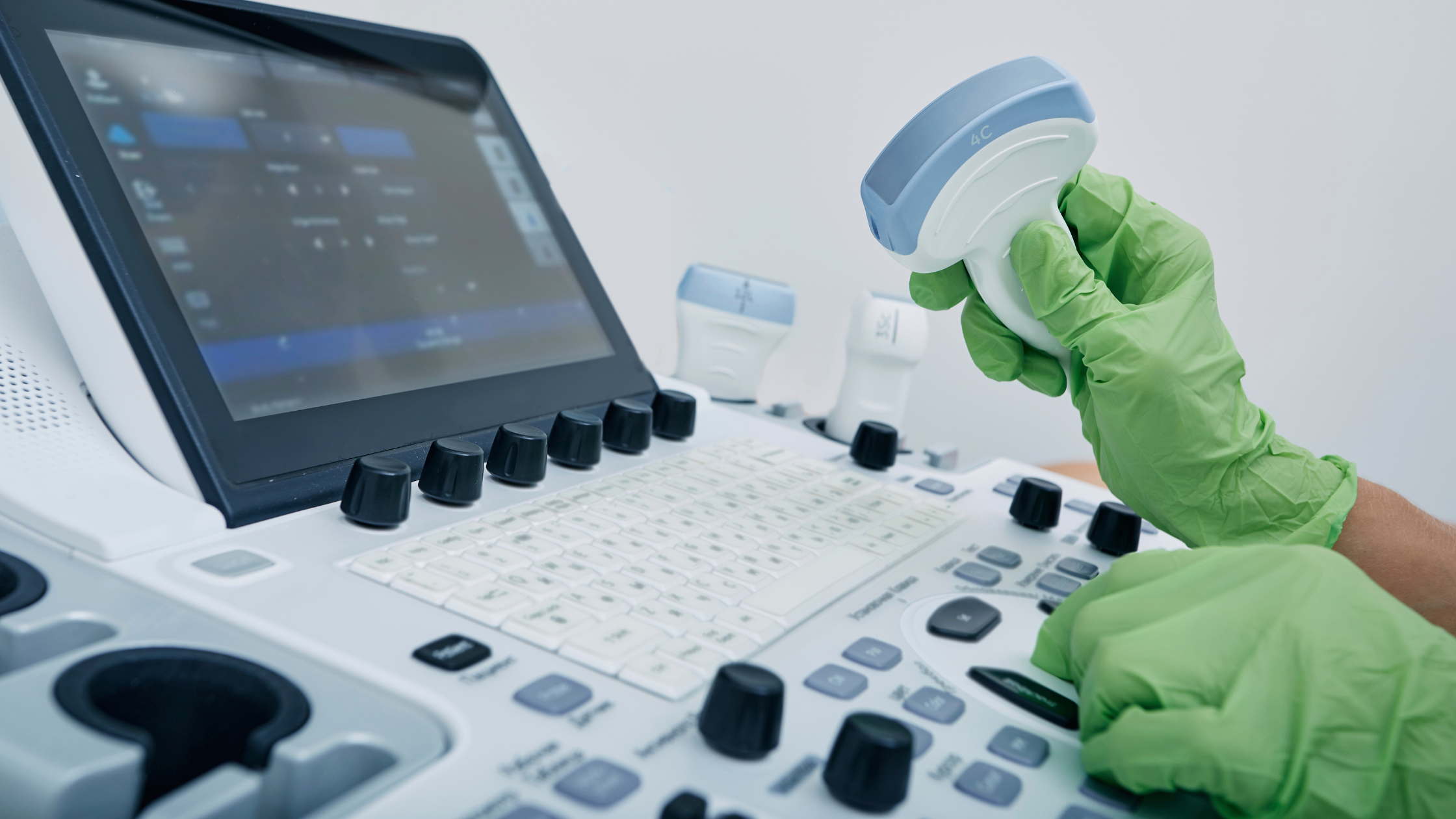 gloved hands holding medical equipment in front of a screen showing data