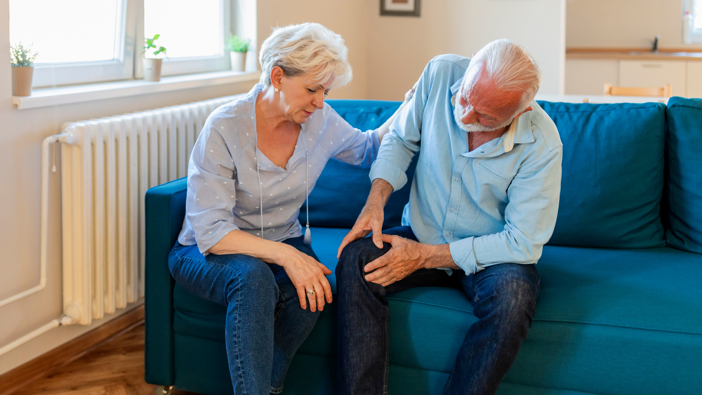 senior woman puts a comforting hand on the should of a senior man who winces and grabs his knee