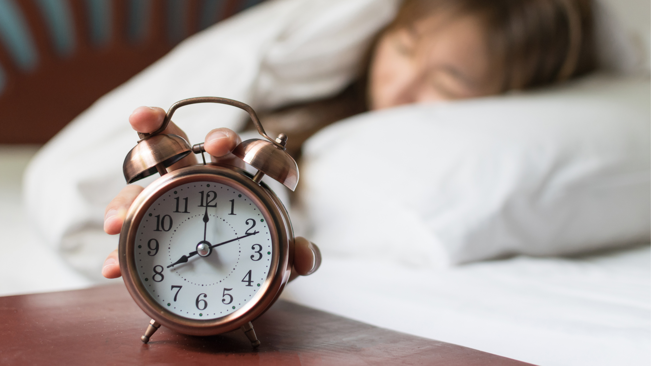 woman reaches out of bed to turn off an old-fashioned alarm clock