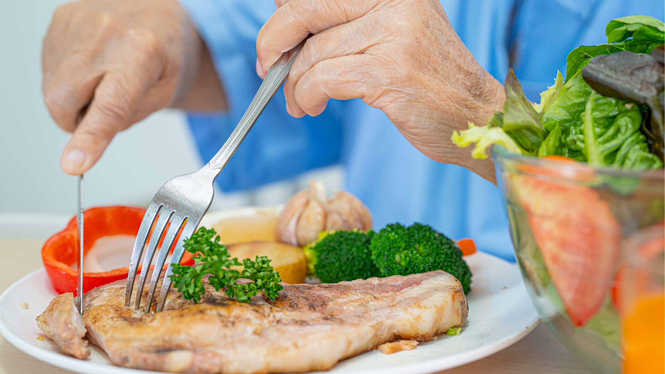 senior cuts up grilled chicken breast on a plate surrounded by veggies