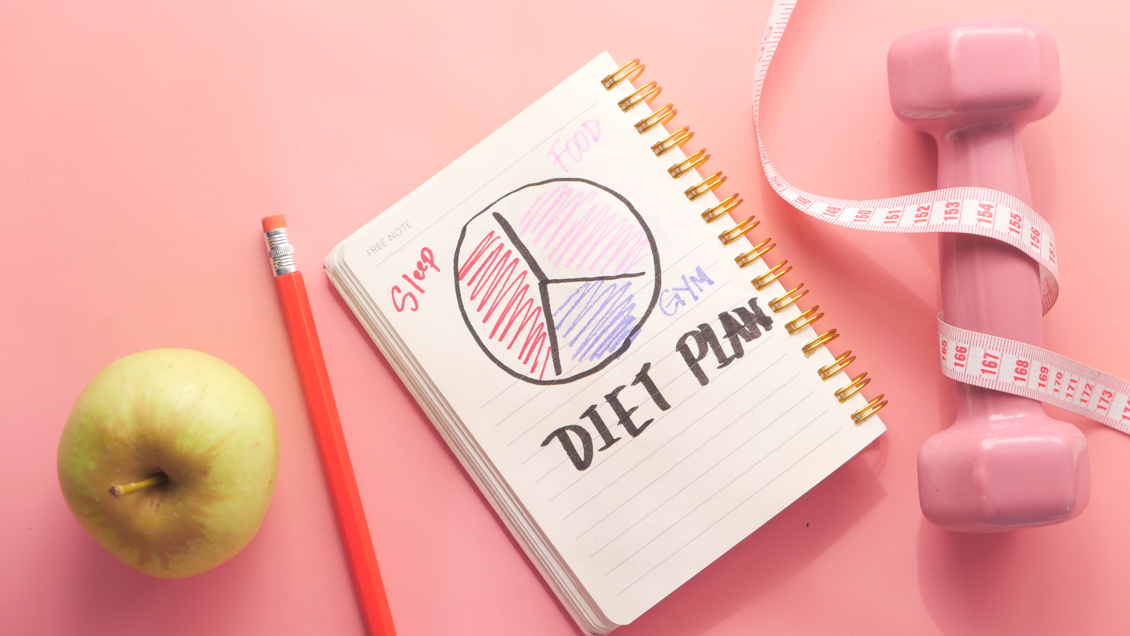 apple, weight, measuring tape, and a notebook saying "diet plan" on a table