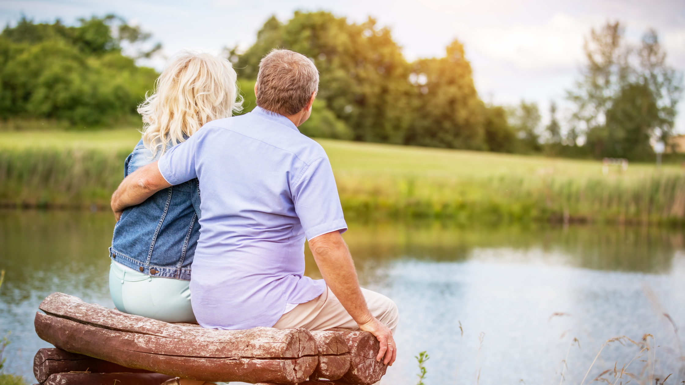 senior couple with their arms around each other, looking over a pond