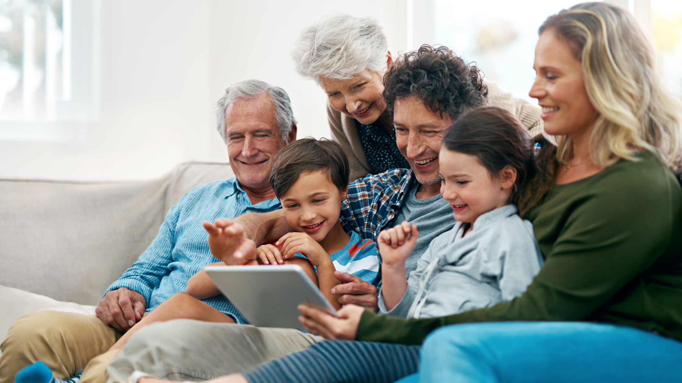multi-generational family sitting on a couch looking at a tablet together