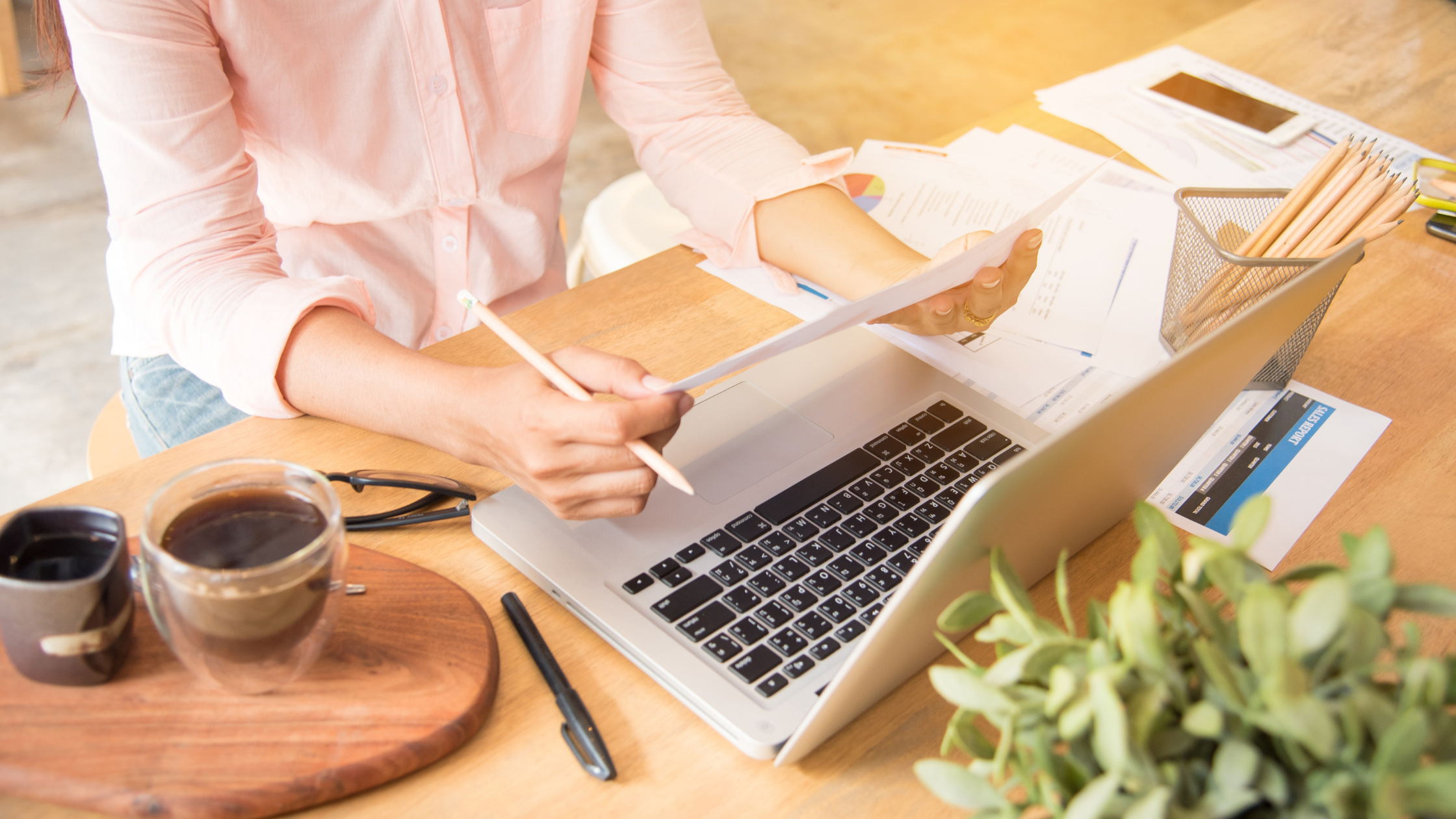 woman sits at a desk covered in paperwork and a laptop