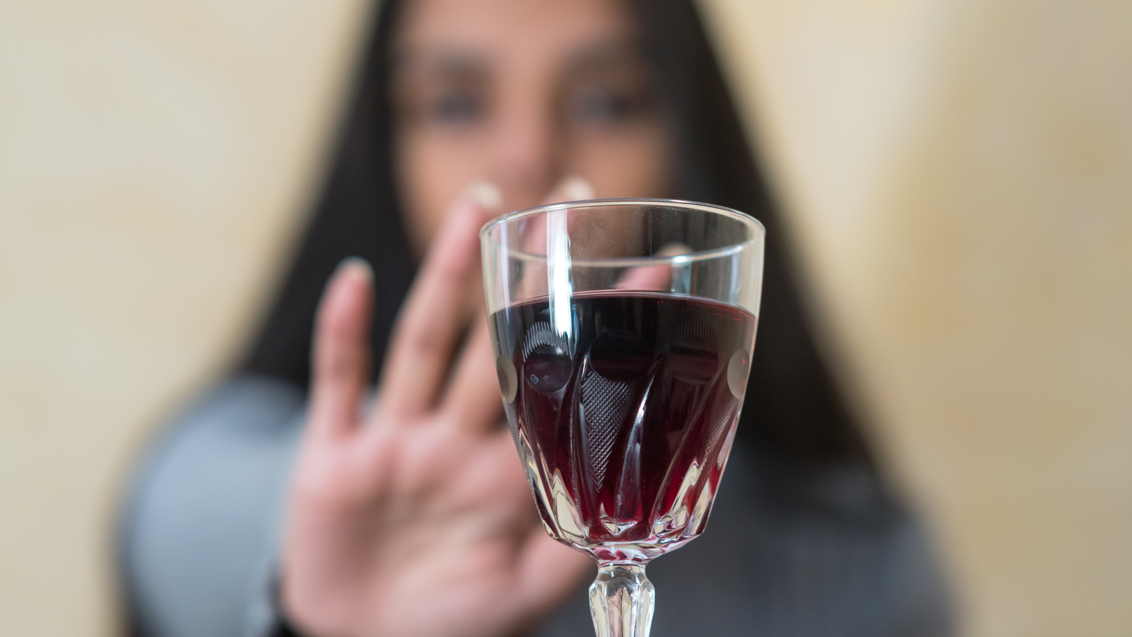 close up of a glass full of wine, with a blurry hand held up in a "no" behind it