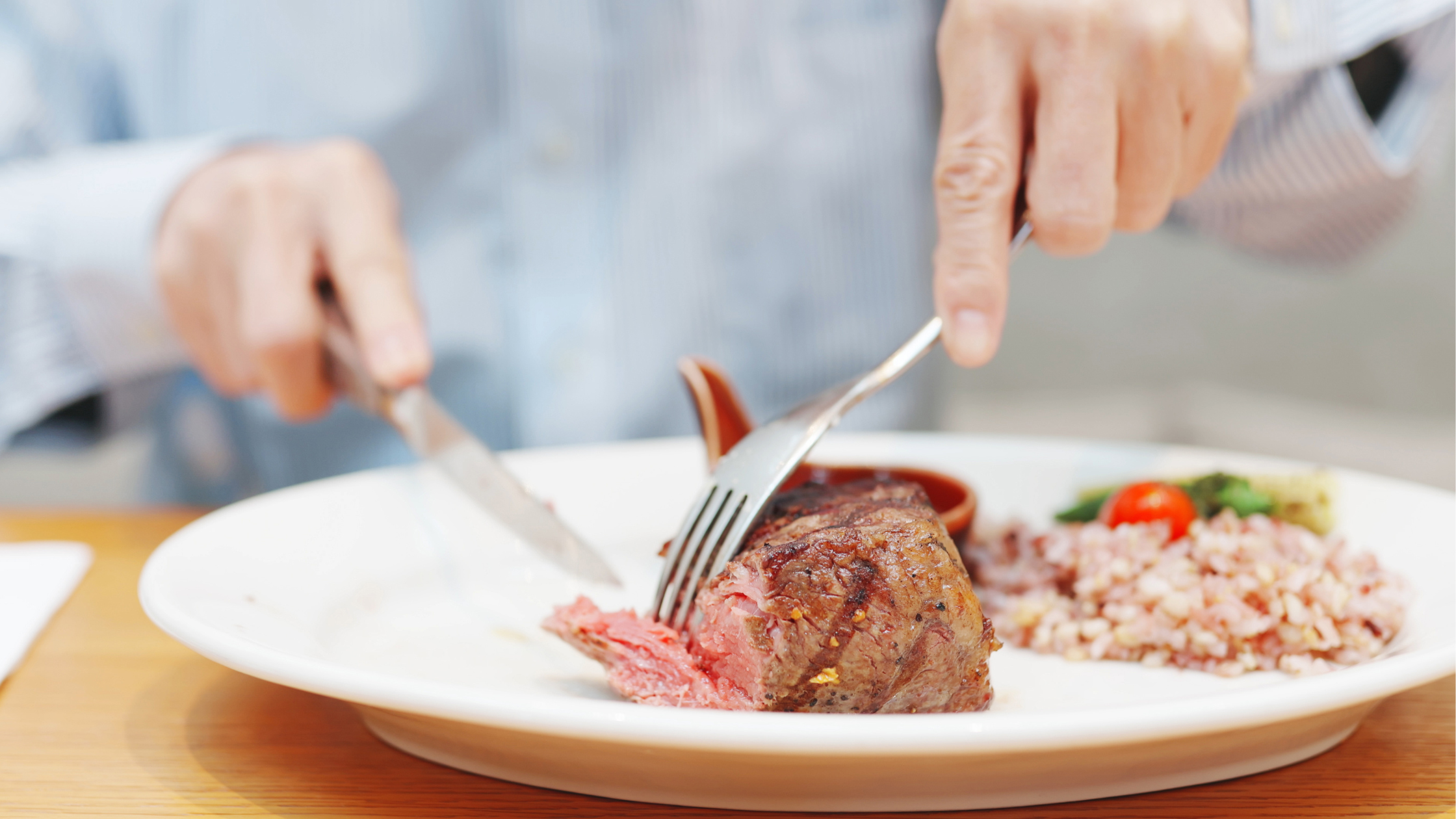 senior cuts the meat of of a drumstick on a plate beside a pile of rice