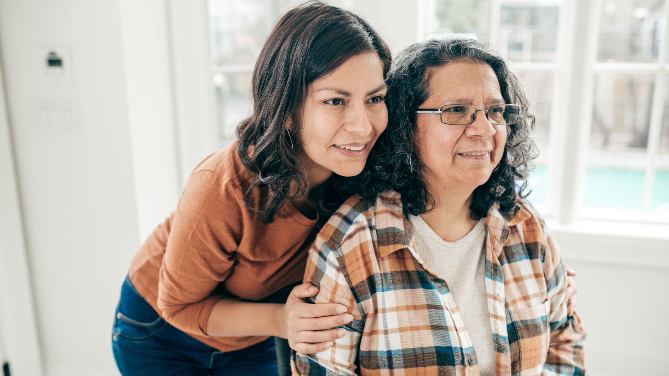 adult daughter embracing senior mother from behind