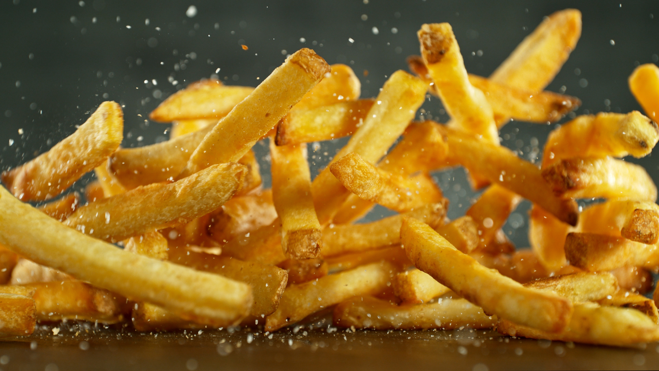 cinematic close up of salty french fries falling into a pile