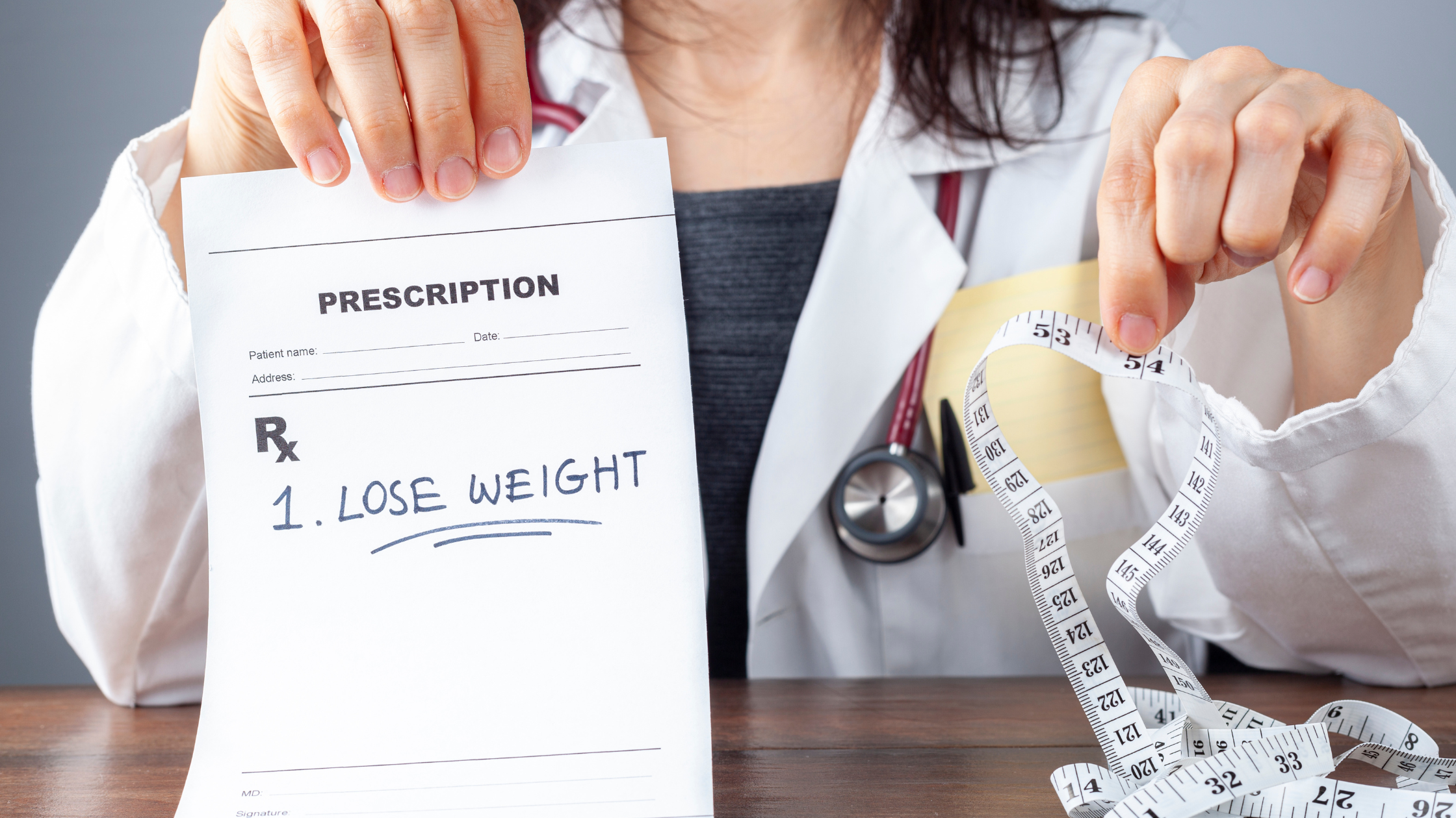 doctor holds up a prescription that says "weight loss" in one hand and a measuring tape in the other