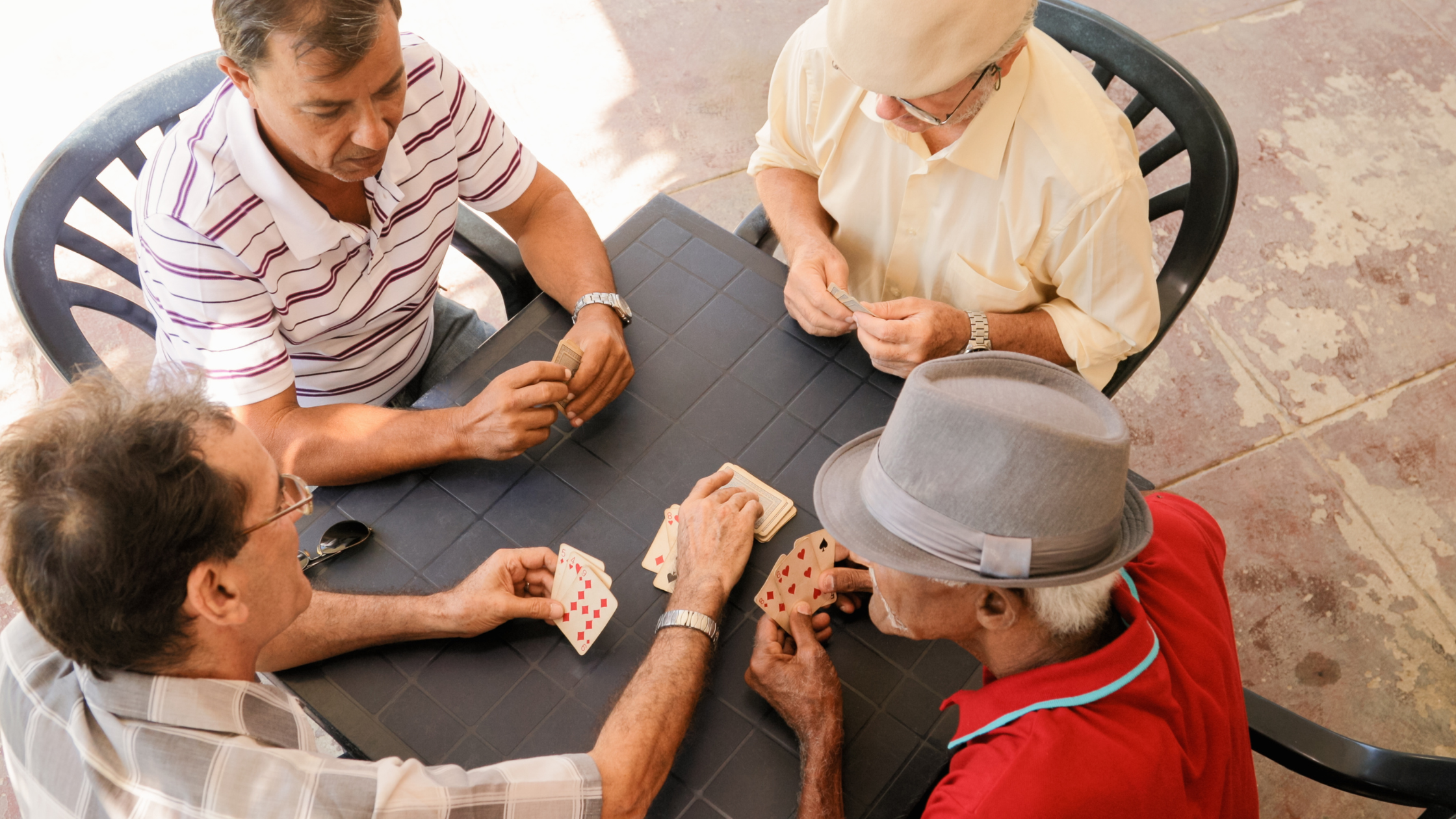 four senior men playing cards around a table