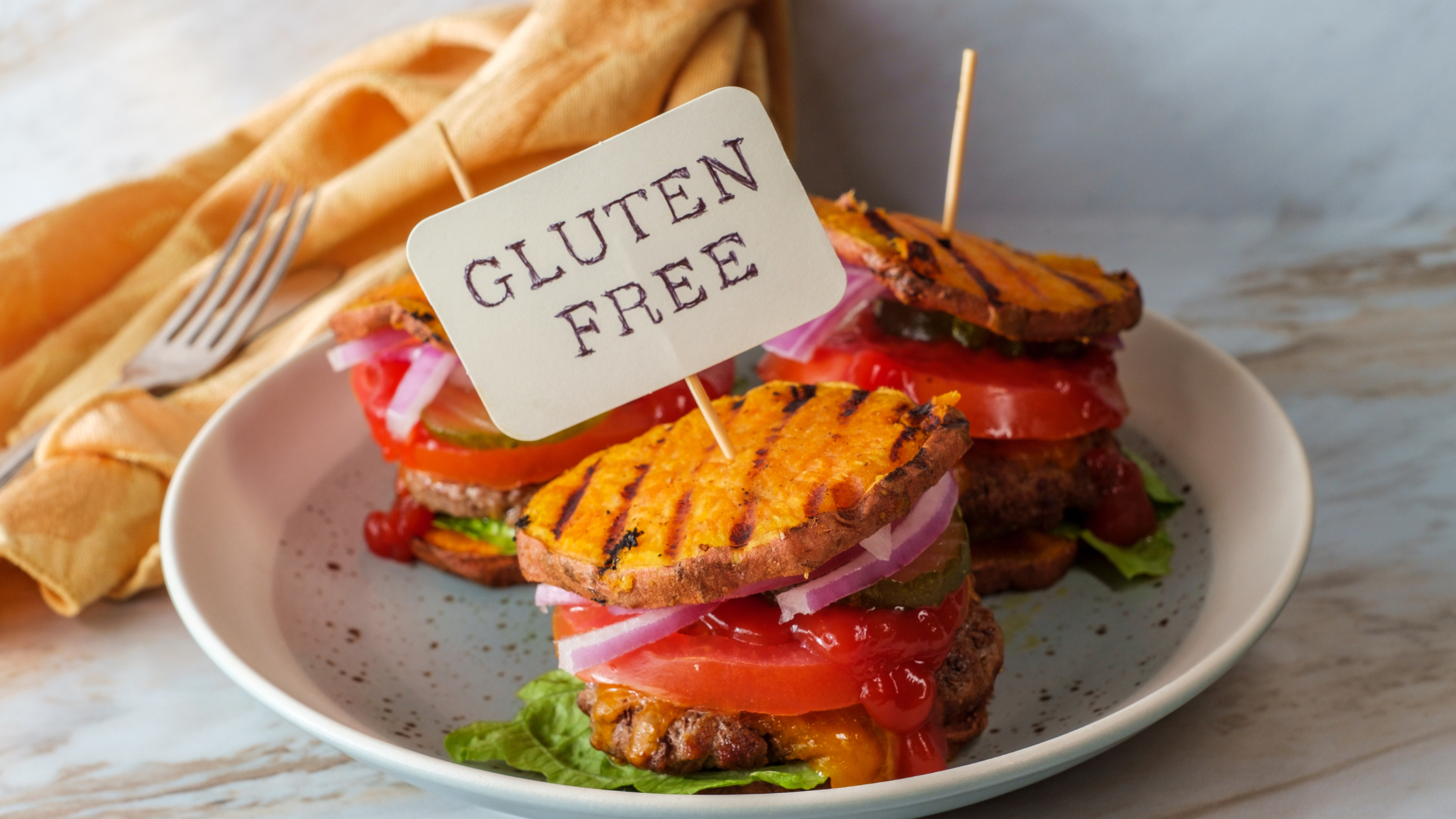 The word "Gluten" drawn in a pile of flour on a wooden table surrounded by various breads, crackers, and dried pastass