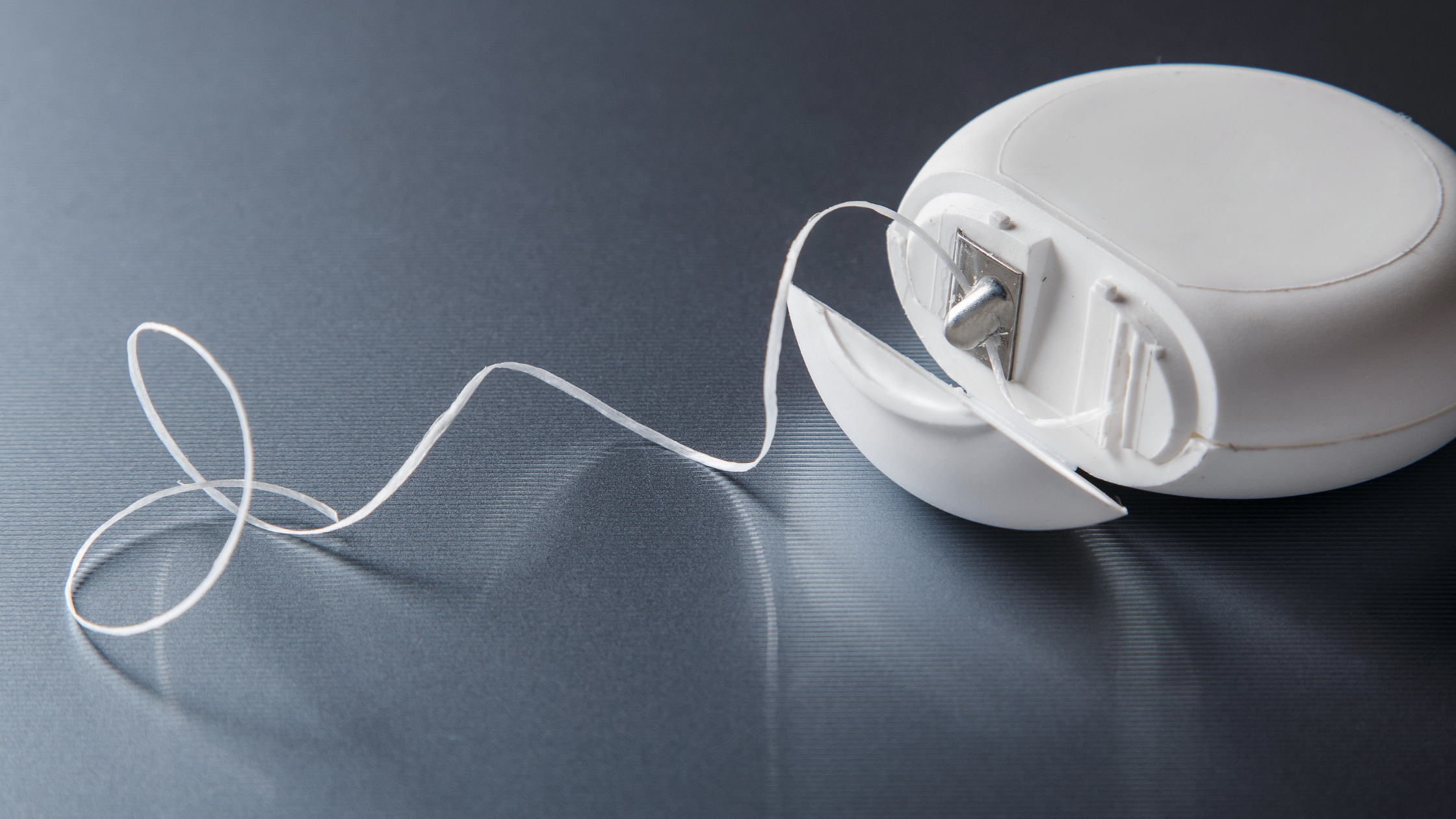round white container of dental floss open on plain background, floss piling out