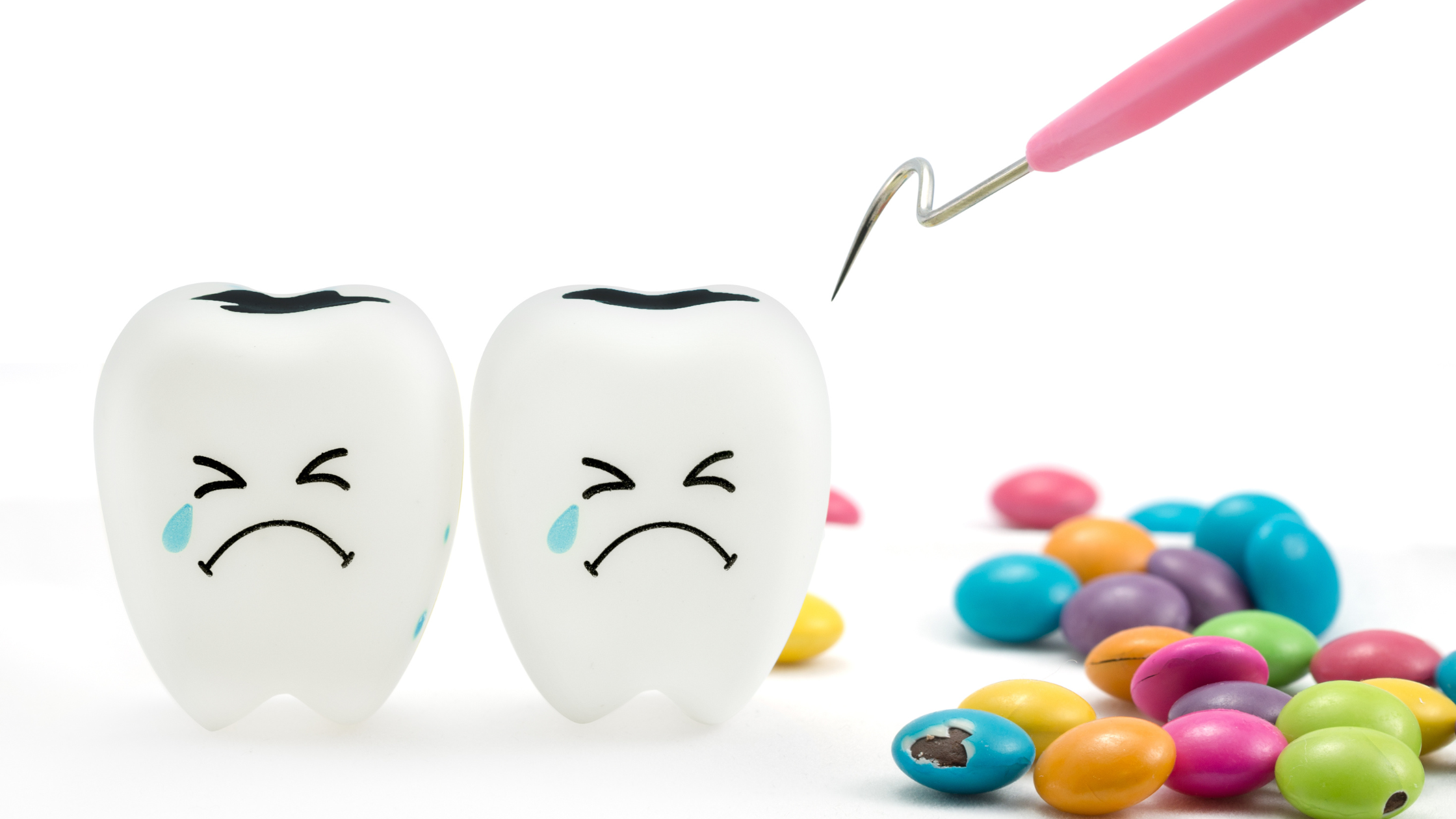 two animated human molars with sad faces cower from a dental tool, colorful chocolate candy sits beside them