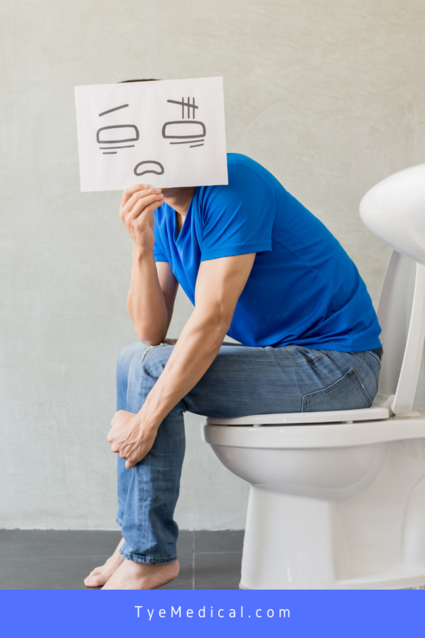 Man sitting on the toilet holding up piece of paper with unhappy face drawn on it