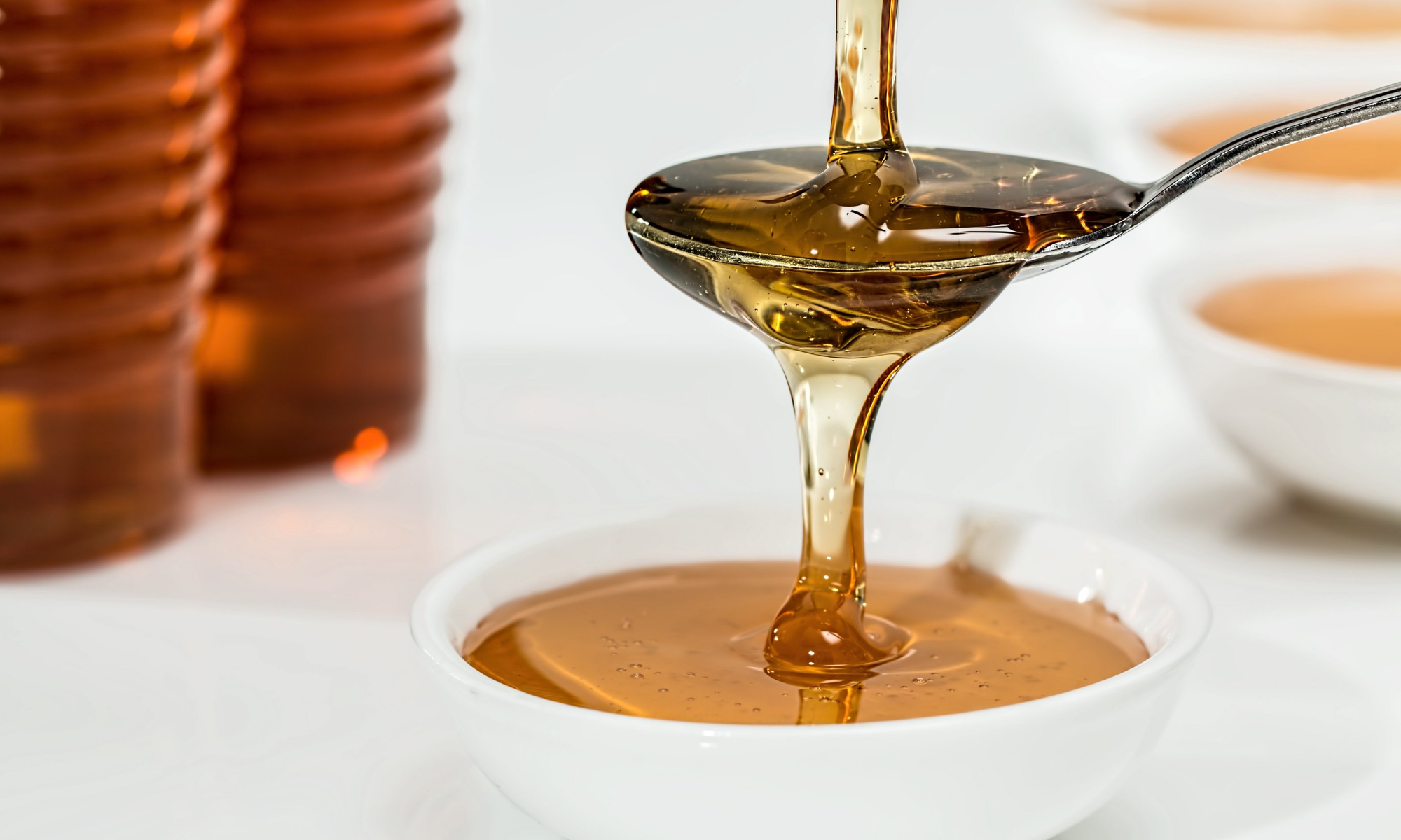 Honey cascading down into a spoon and overflowing into a small bowl