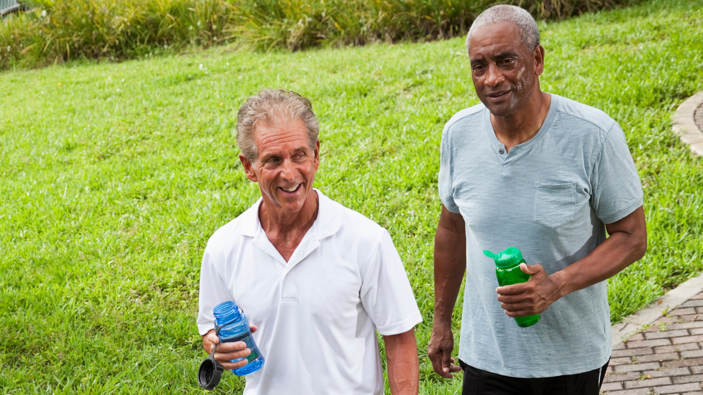 Two smiling older men outside sweating after a workout with bottles of water in their hands