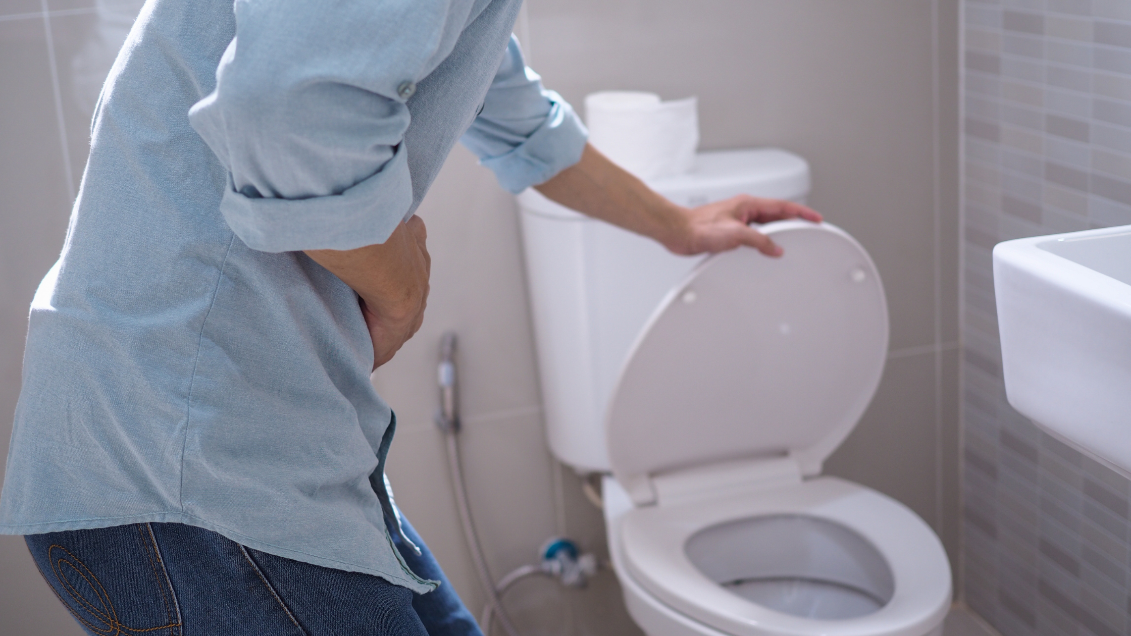 person clutching their lower abdomen as they open the toilet lid