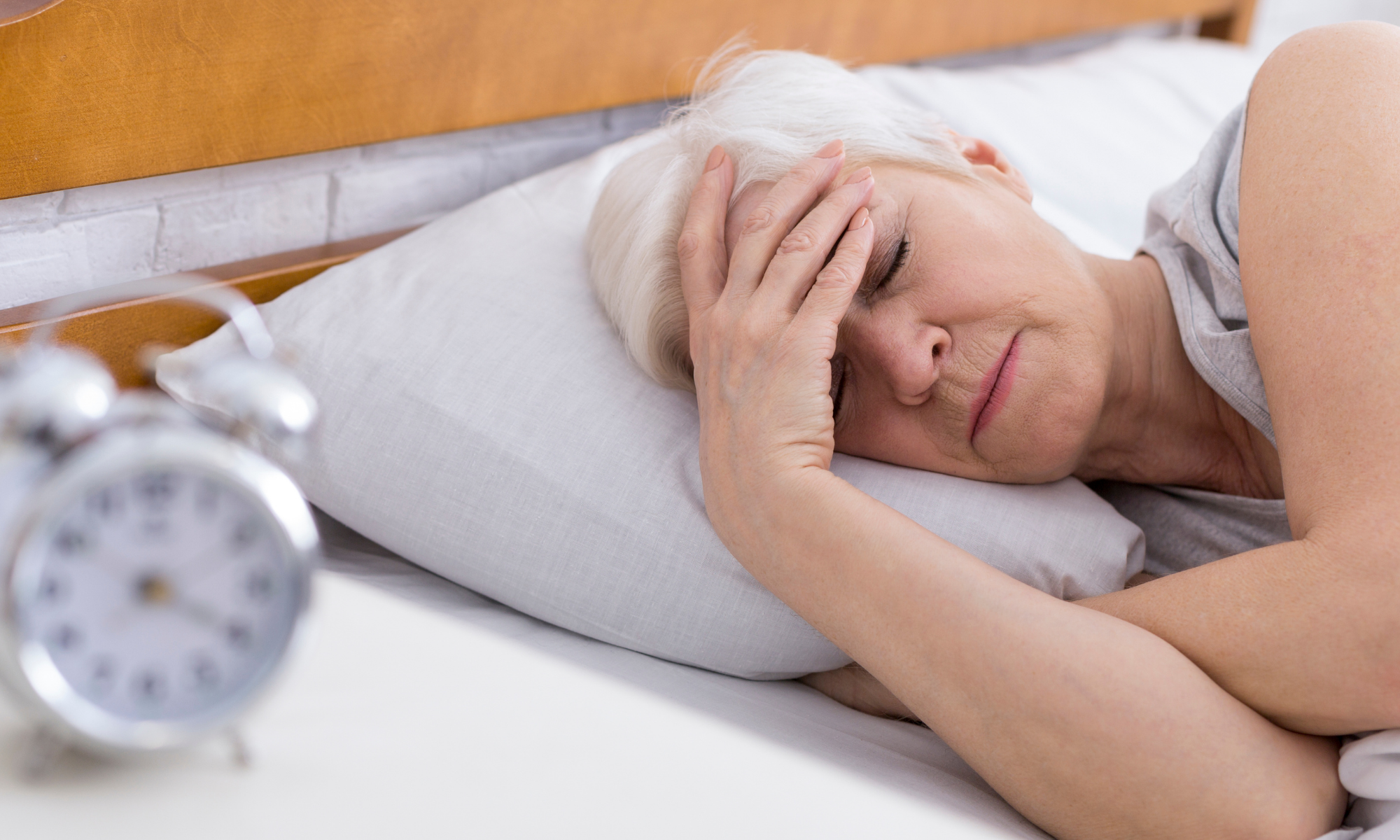 Senior woman in bed with headache, morning but doesn't want to get out of bed
