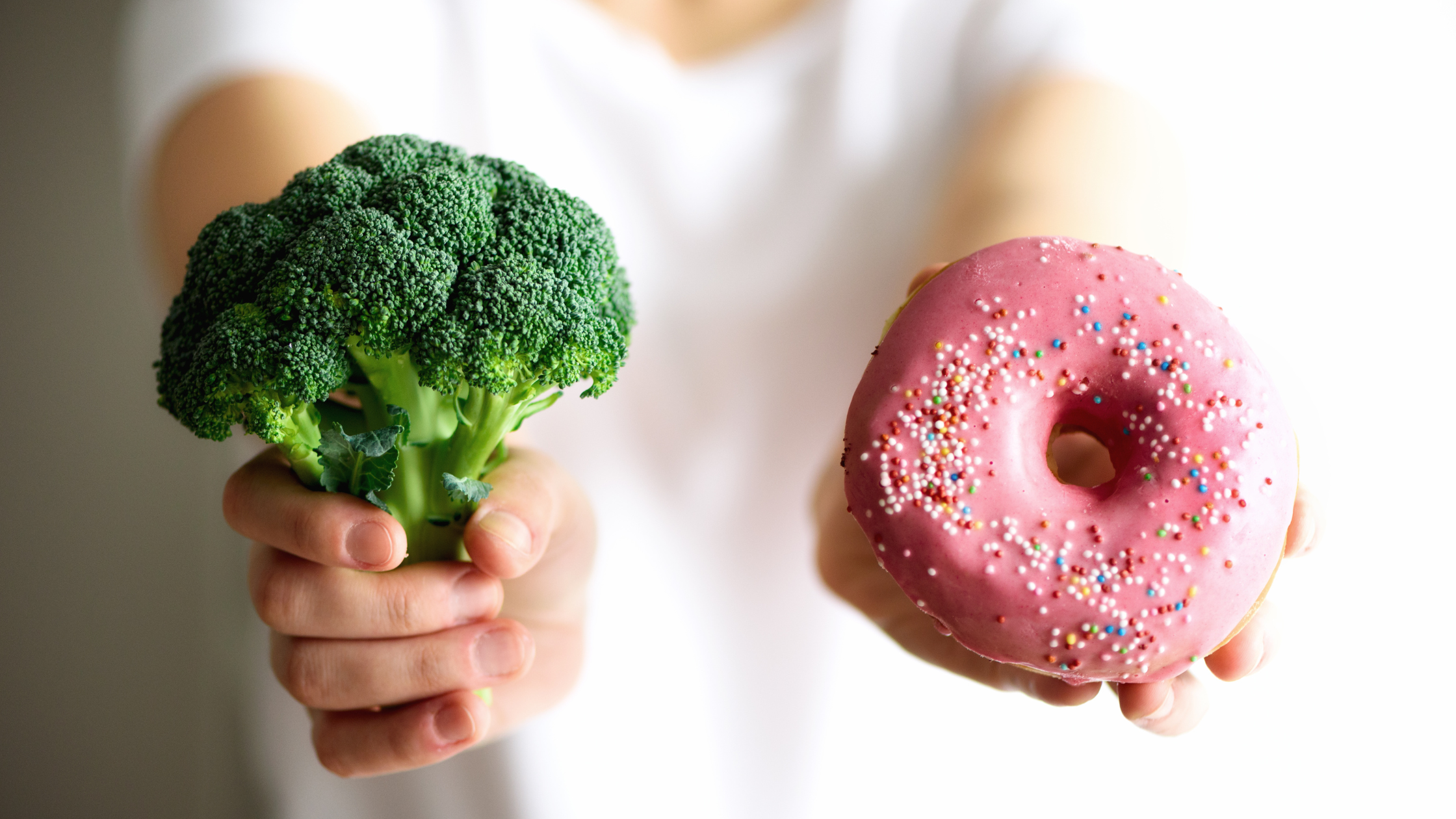 two hands out, one holds broccoli and the other a donut