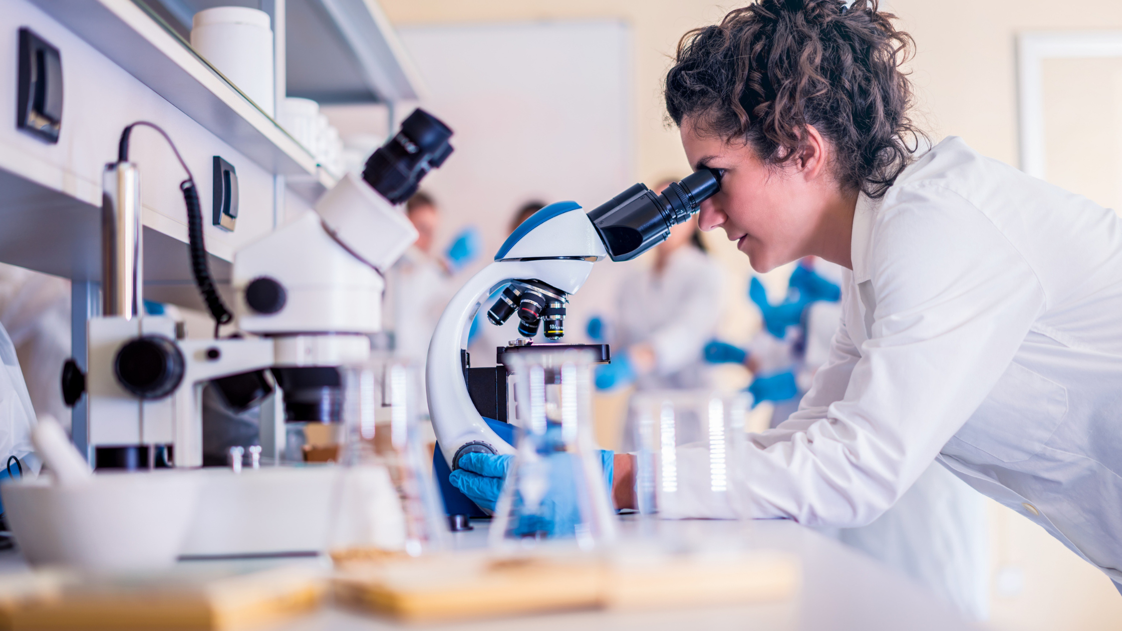 woman in a lab coat looks through a microscope