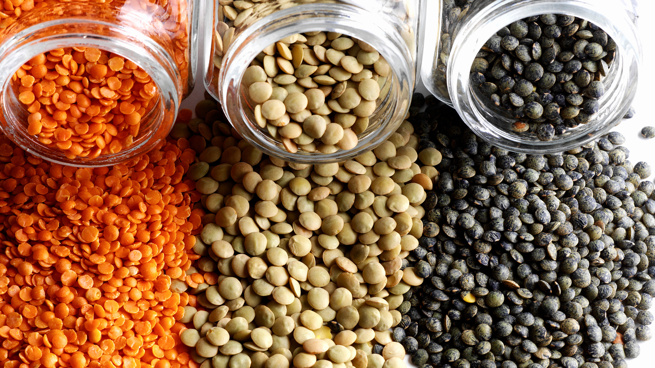 three open jars with three different colors of beans spilling out