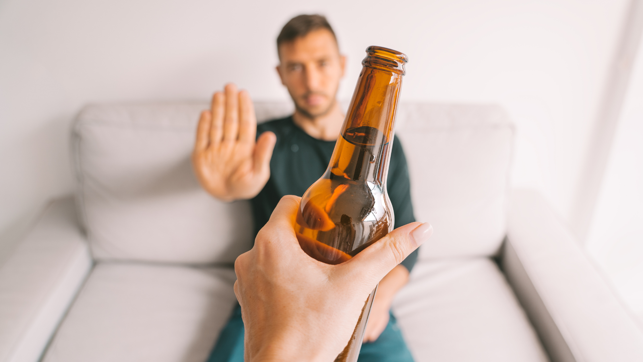 adult holding up their hand to refuse an offered bottle of beer