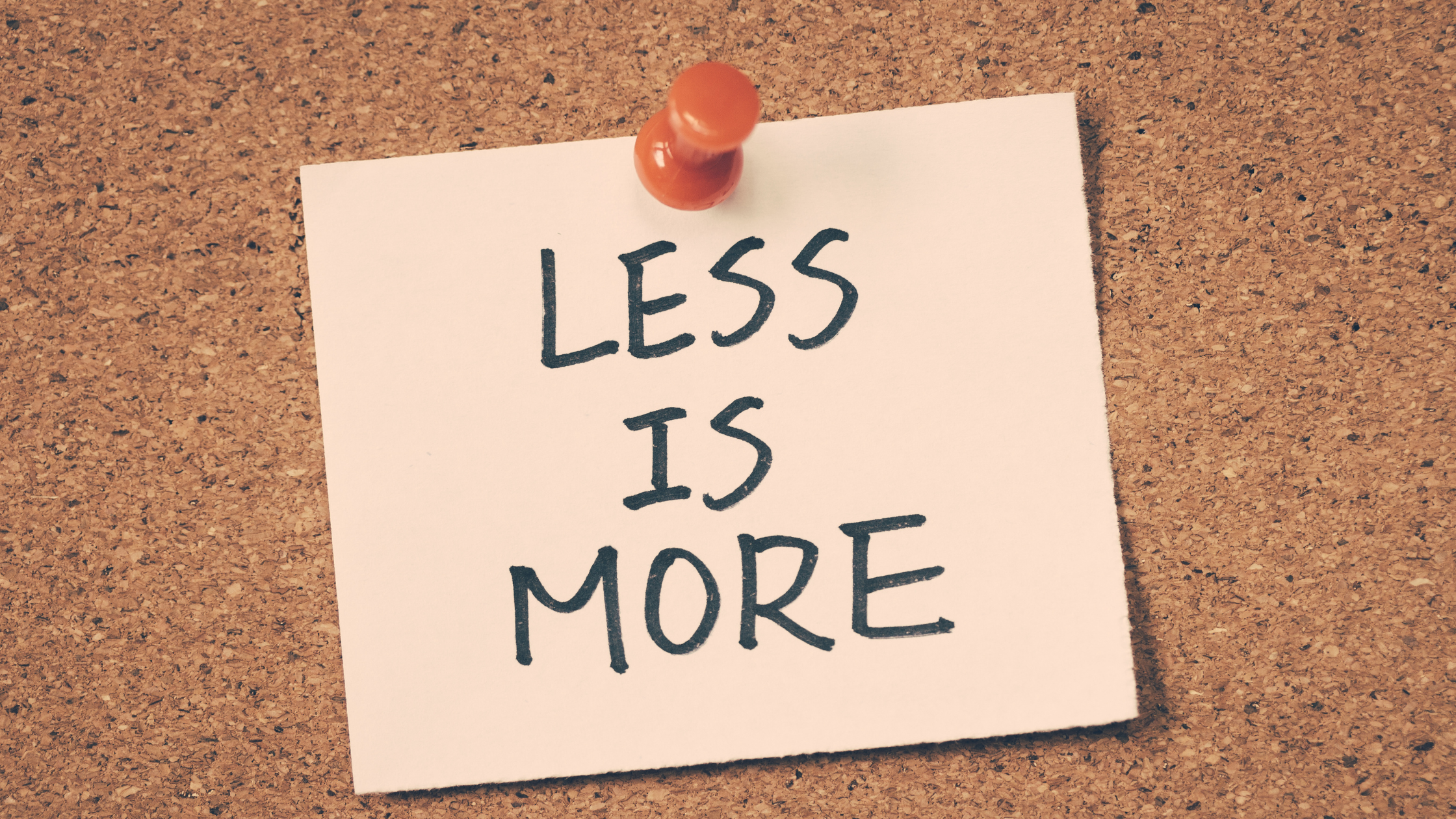 note saying "less is more" pinned to a corkboard